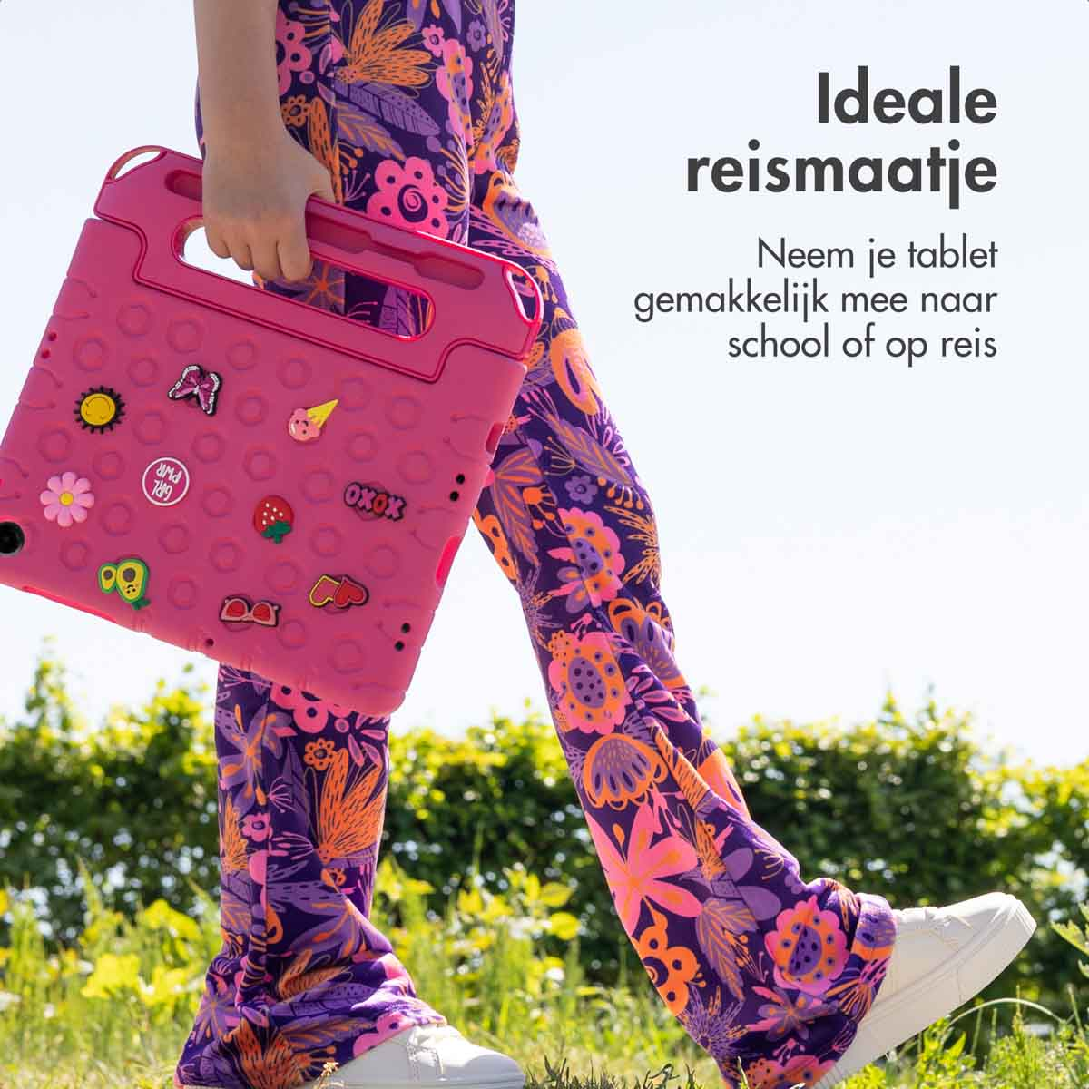 A child holding a pink tablet case with stickers, standing in a field of flowers.