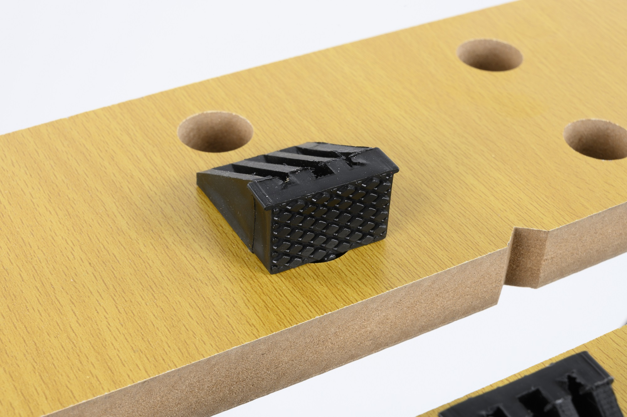 Een close-up van een houten werkbank met zwarte rubberen stopper en drie gaten.
