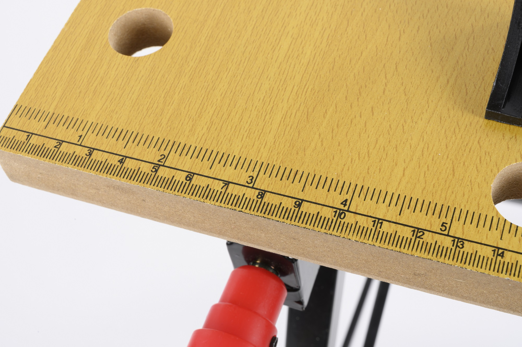 Close-up van een houten werkbank met een liniaal en gaten. Zwarte metalen poten zijn zichtbaar. Witte achtergrond.