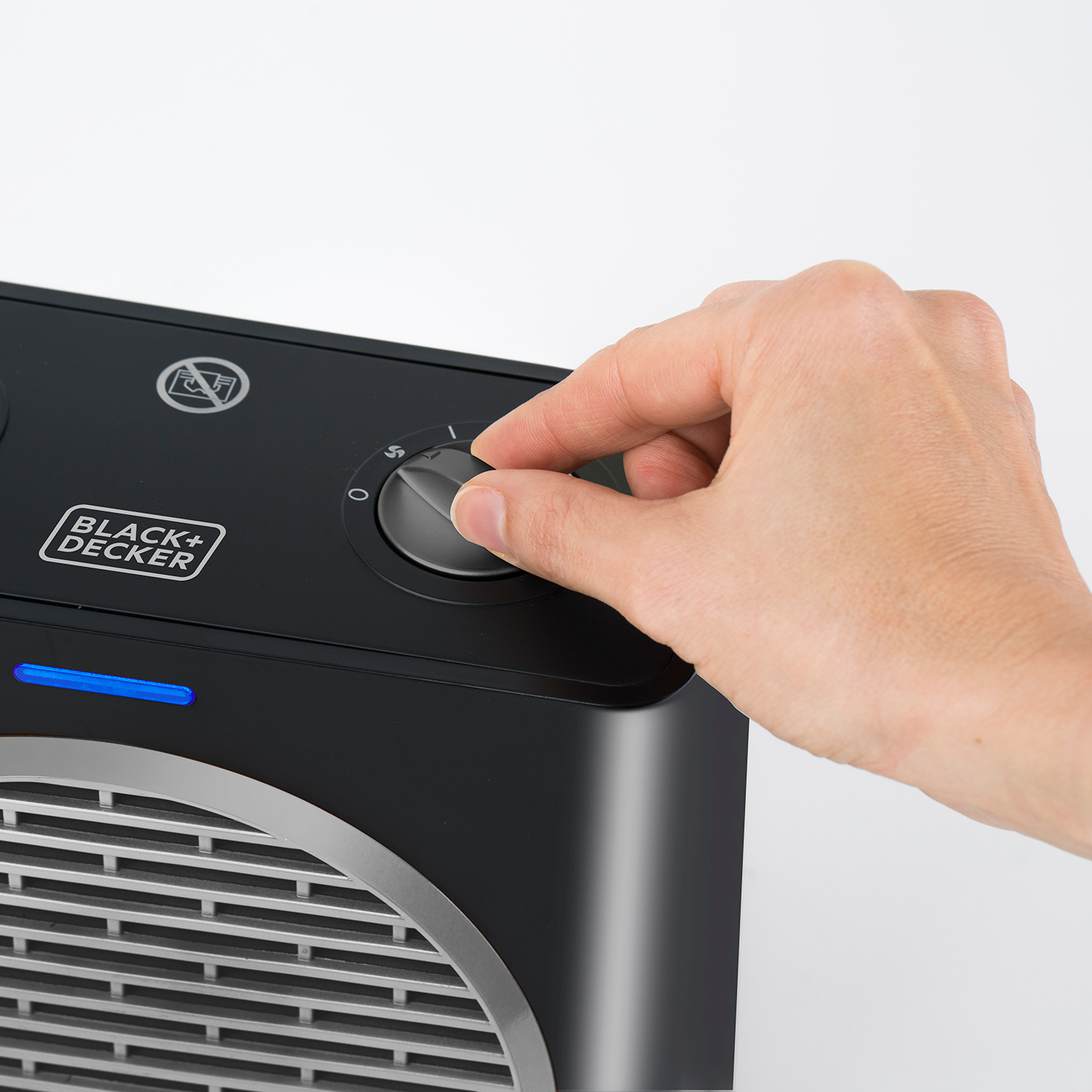 Dłoń przekręcająca pokrętło grzejnika Black+Decker. Białe tło.