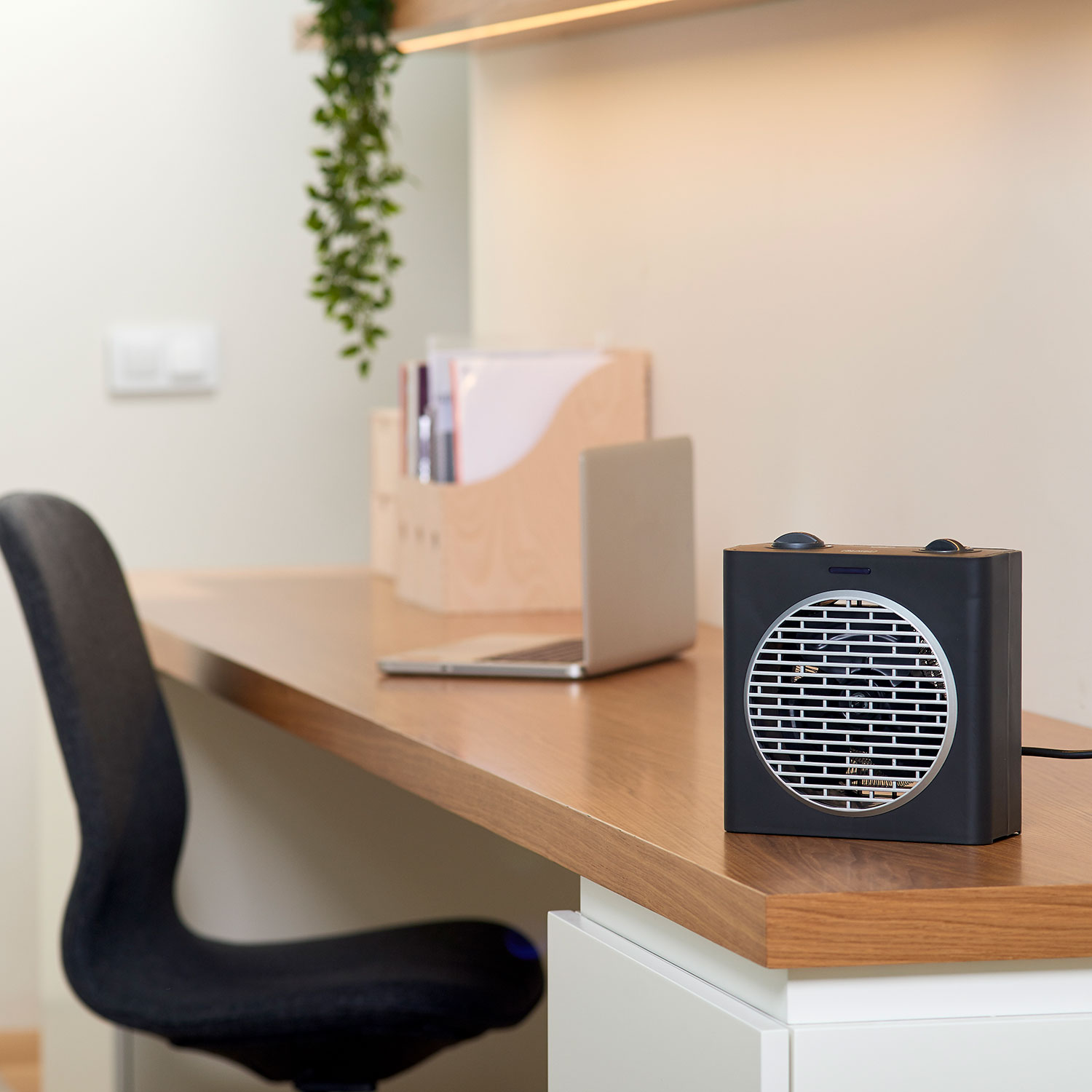 Czarny grzejnik na drewnianym biurku obok laptopa i wiszącej rośliny. Ustawienie wnętrza.