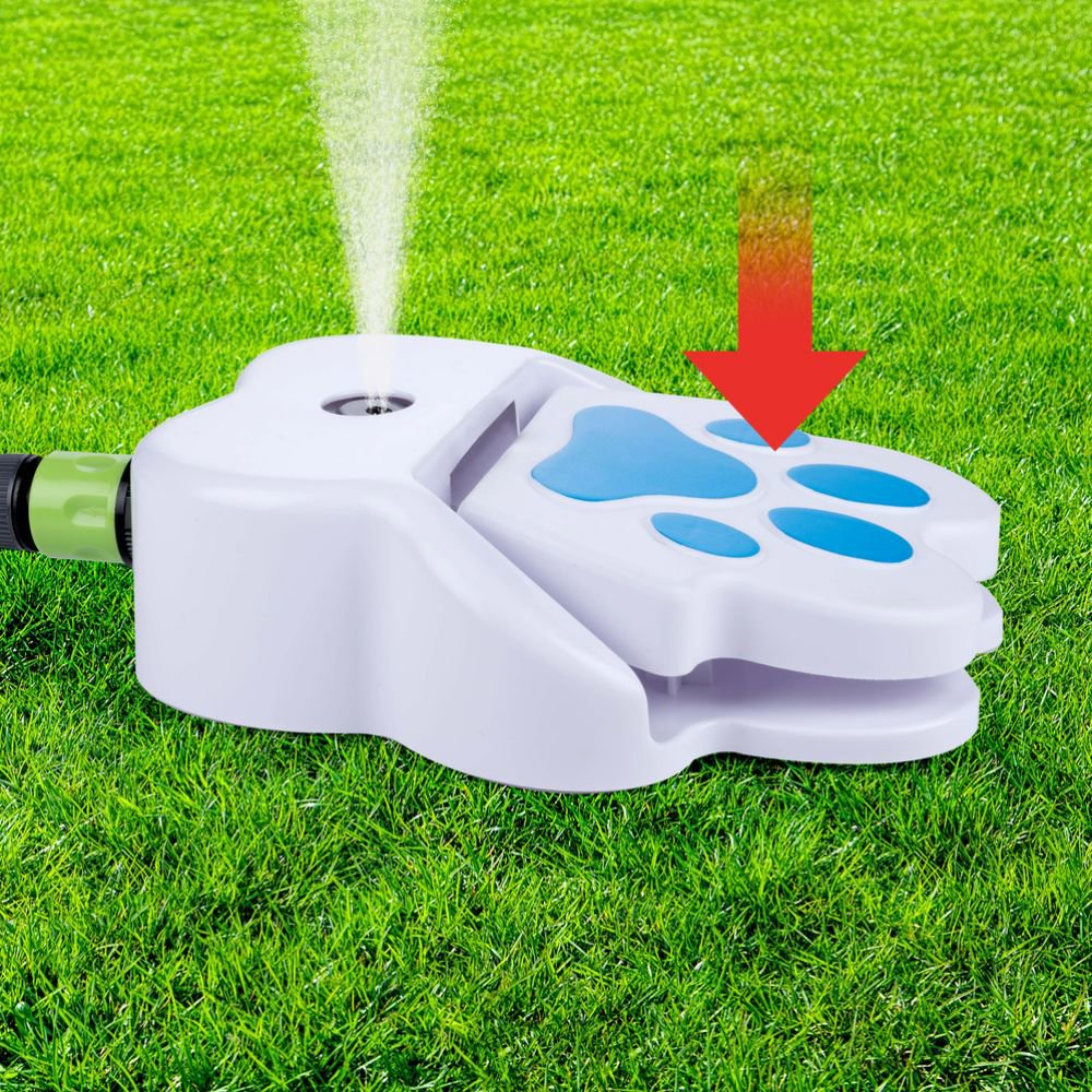 Dog paw-shaped sprinkler on grass, water spraying. Red arrow indicates the foot-shaped pedal.