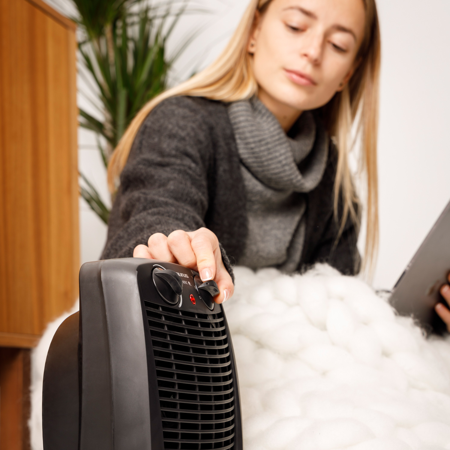 Kobieta reguluje ustawienia temperatury na czarnym grzejniku Taurus, używając tabletu i koca.