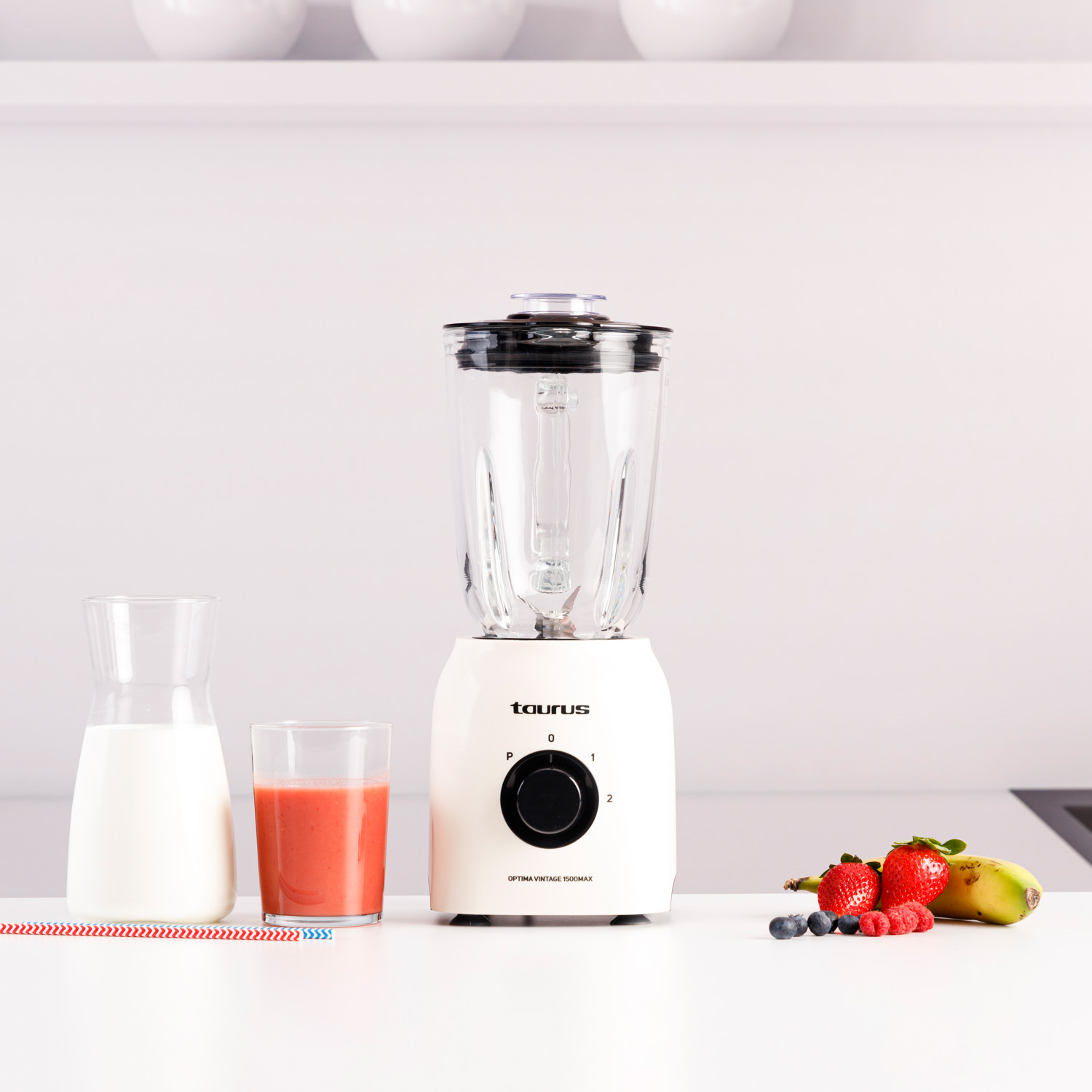 Ein weißer Mixer auf einer Arbeitsplatte mit einem Smoothie-Glas, Milch und Früchten daneben.