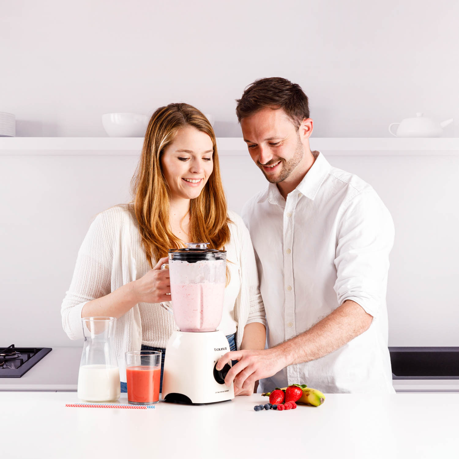 Ein Paar in einer Küche, das mit einem Mixer einen Smoothie zubereitet, Zutaten auf der Theke.