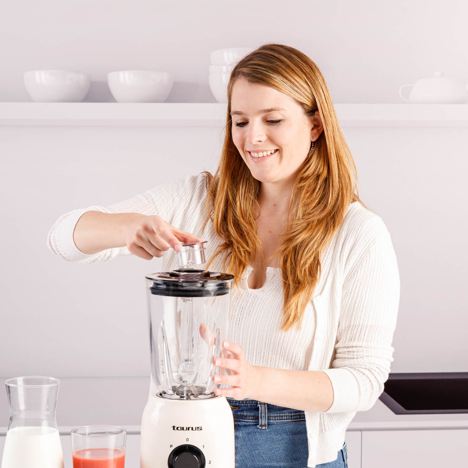 Frau bereitet einen Smoothie zu, hält den Deckel eines Mixers auf einer weißen Arbeitsplatte.