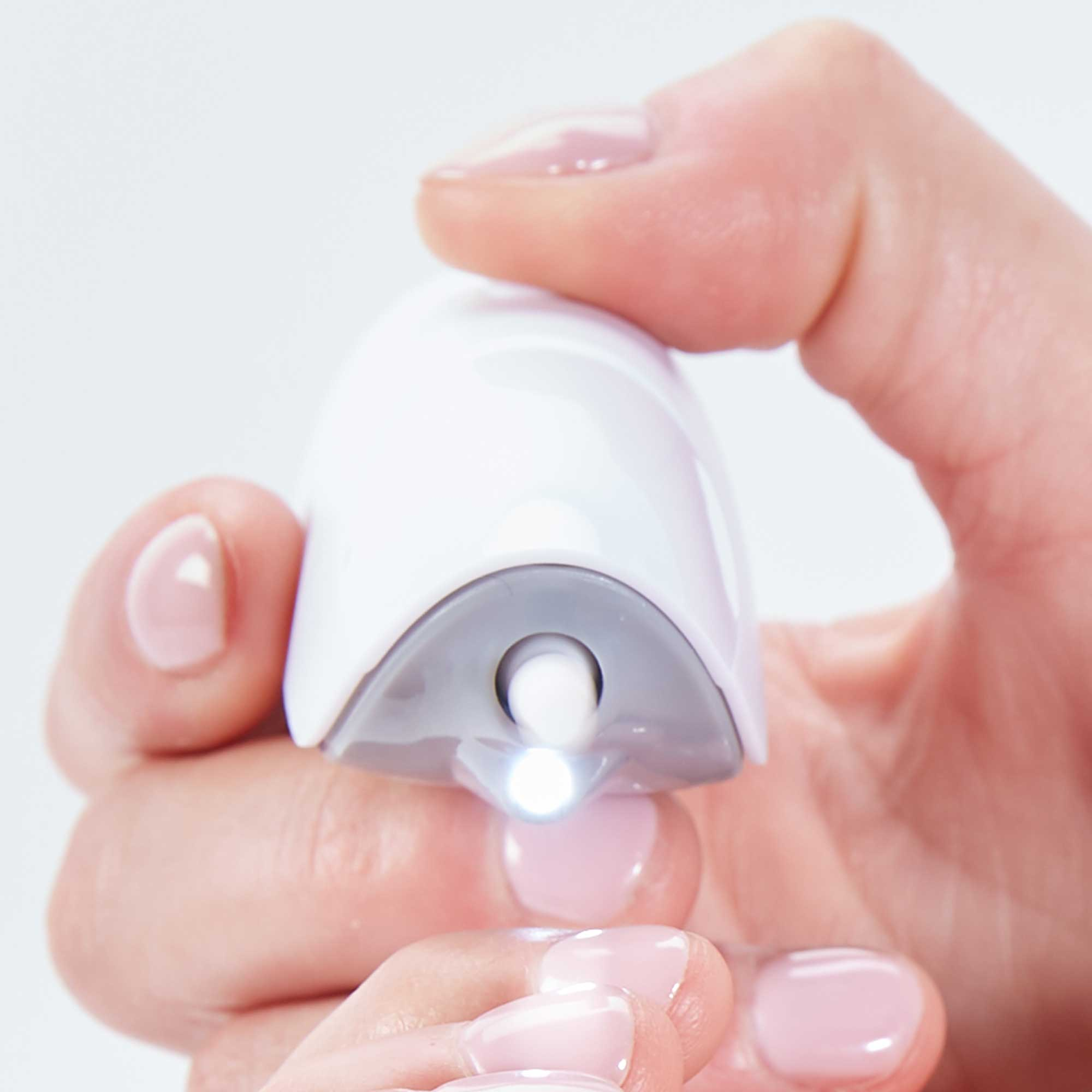 Dłoń trzymająca białe urządzenie do pielęgnacji paznokci z małym światłem. Różowy lakier do paznokci.