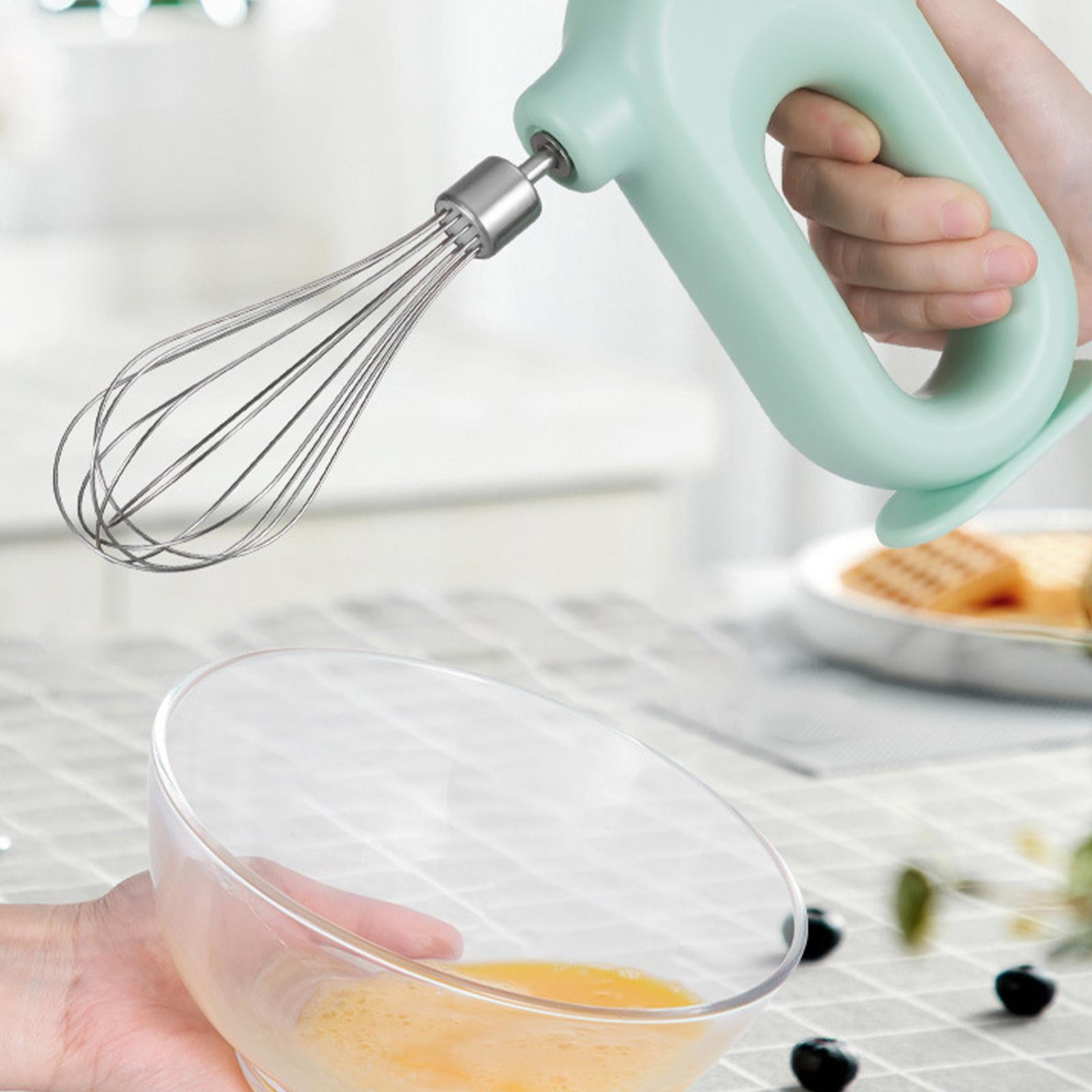 Eine Hand verrührt Eigelb in einer Glasschüssel mit einem hellgrünen Handmixer.