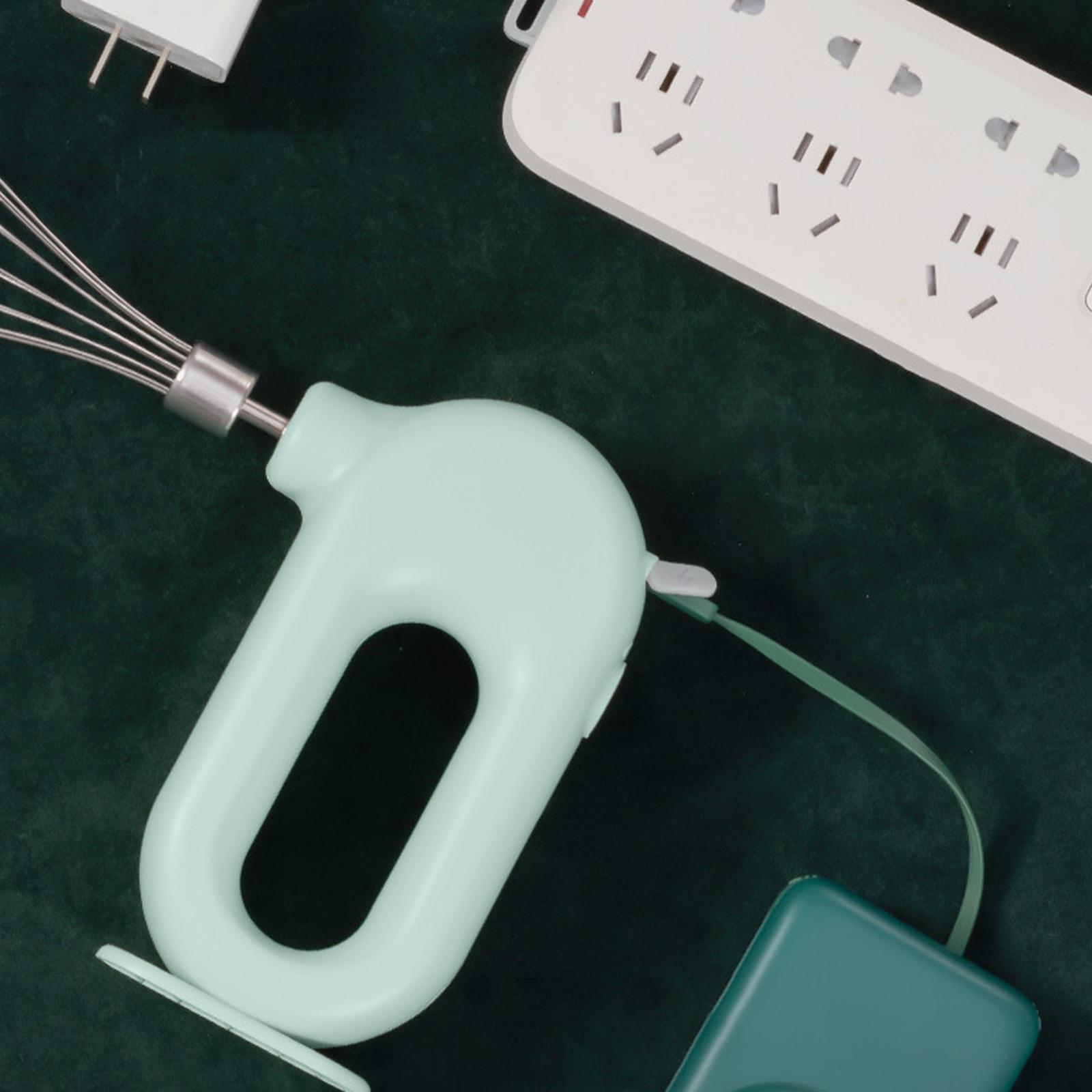 Hellgrüner Handmixer mit grünem Kabel und Ladeanschluss auf dunkelgrüner Oberfläche.