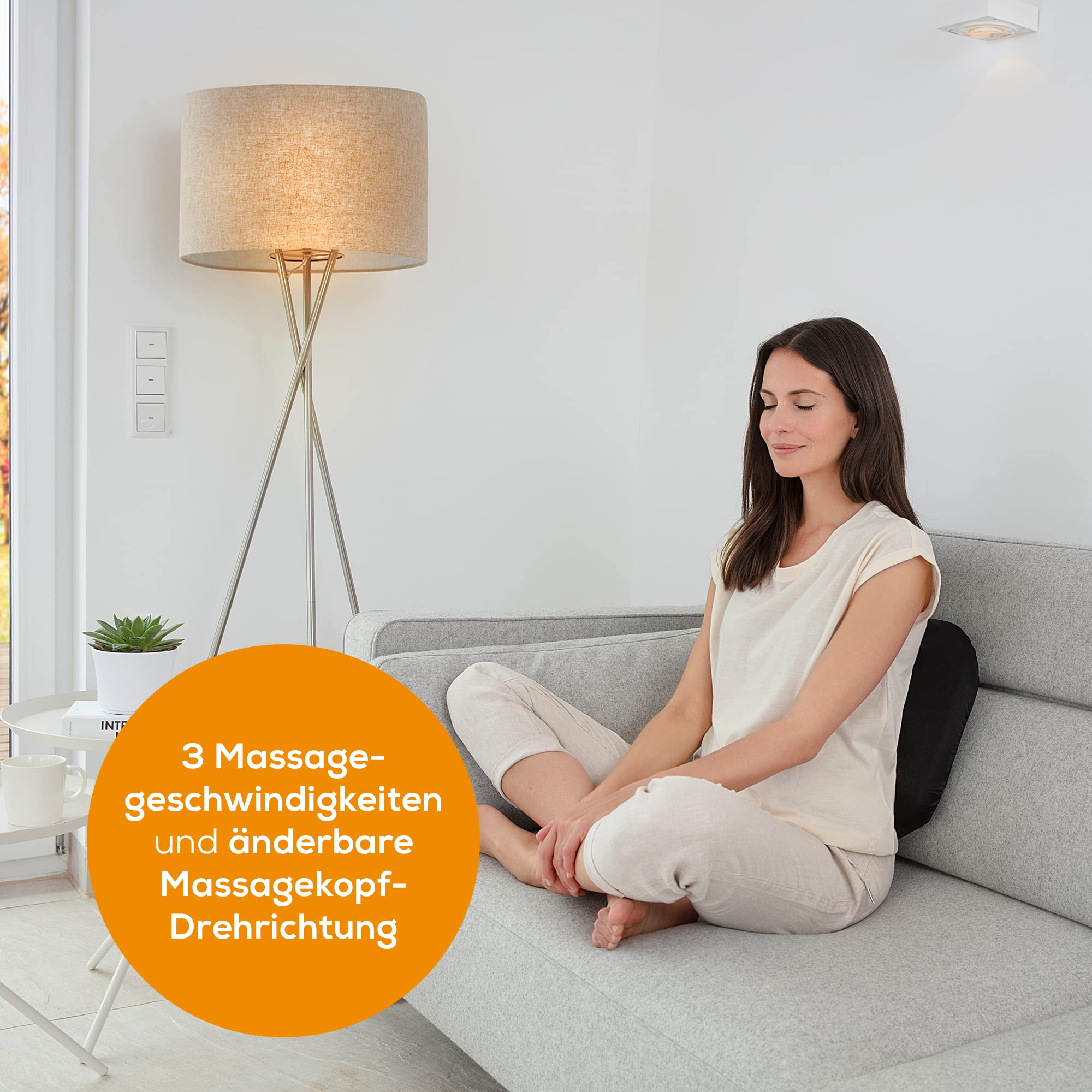 Frau sitzt auf einem grauen Sofa mit schwarzer Rückenstütze. Eine Stehlampe ist links.