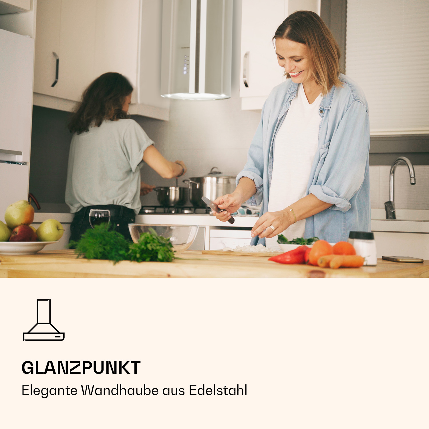Frau in der Küche schneidet Gemüse, daneben eine andere Frau und Dunstabzugshaube.