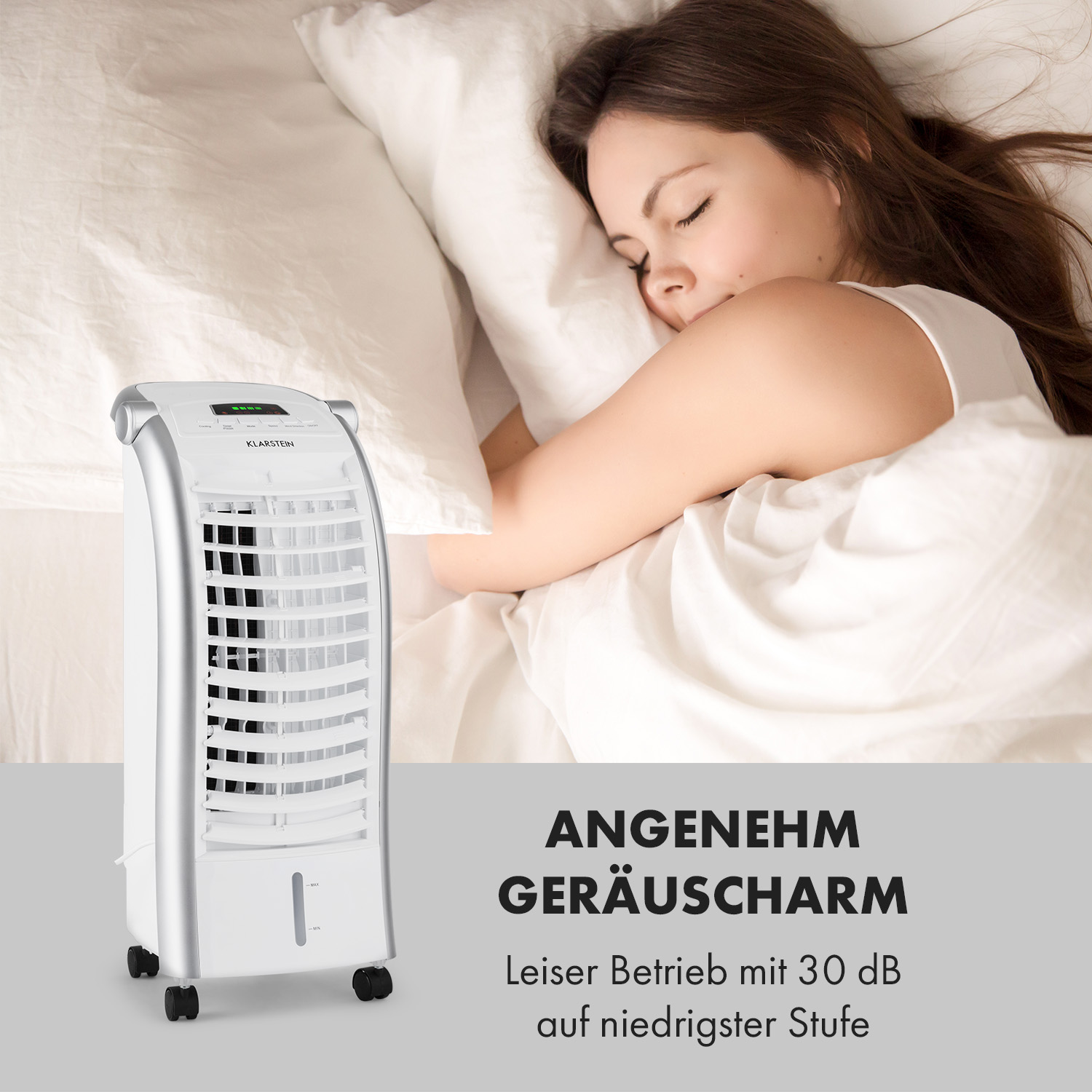 Eine Frau schläft im Bett neben einem weißen Luftkühler, der auf Rädern steht.