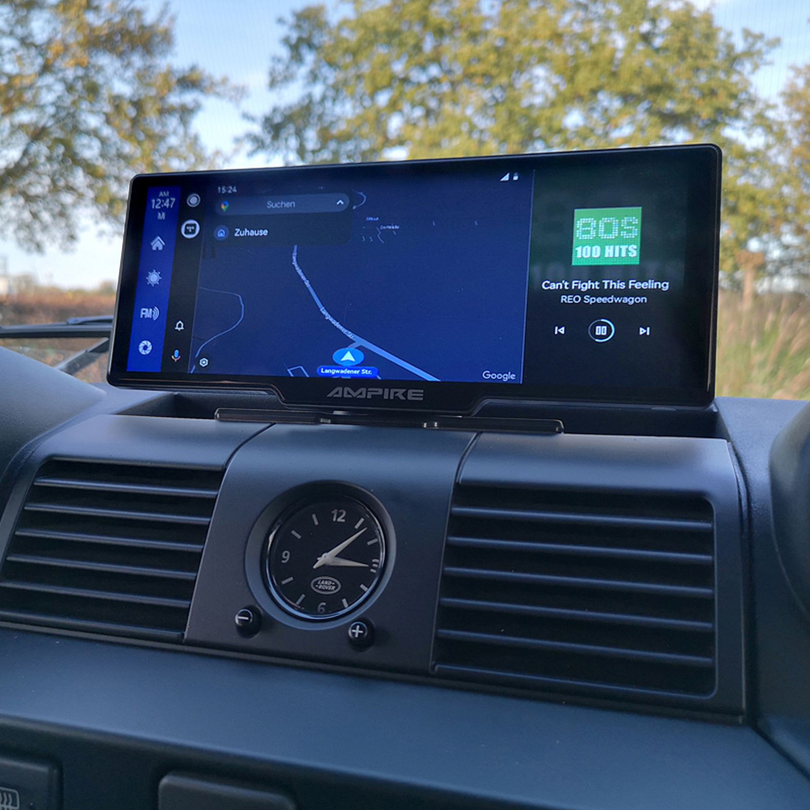 Ein Auto-Infotainment-Bildschirm mit Navigationskarte und Musiksteuerung. Es ist in einem Auto. Eine Uhr und Luftauslässe sind sichtbar.