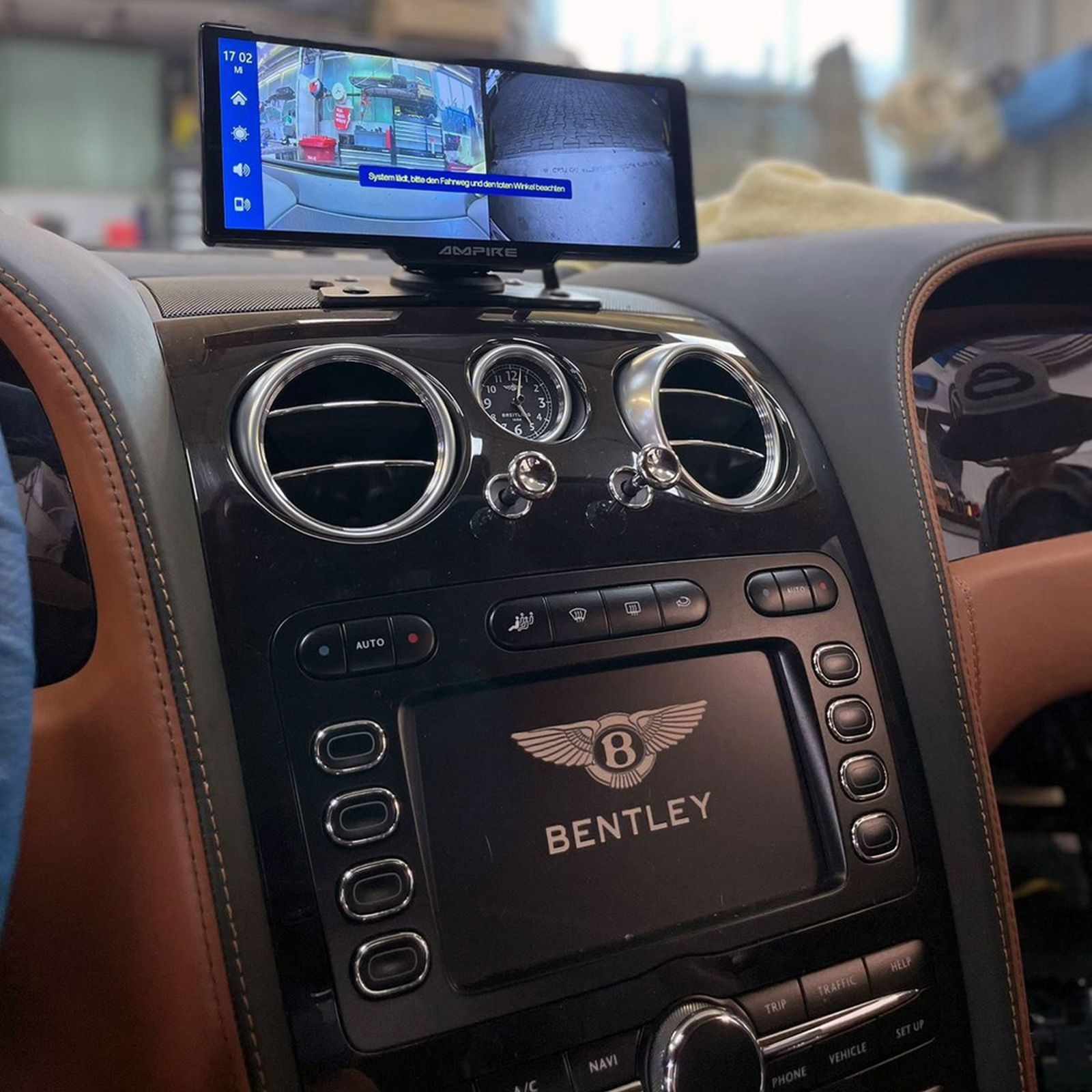 Autoinnenraum mit Bildschirm, der ein Geschäft zeigt. Das Armaturenbrett hat ein Bentley-Logo. Braunes und schwarzes Interieur.