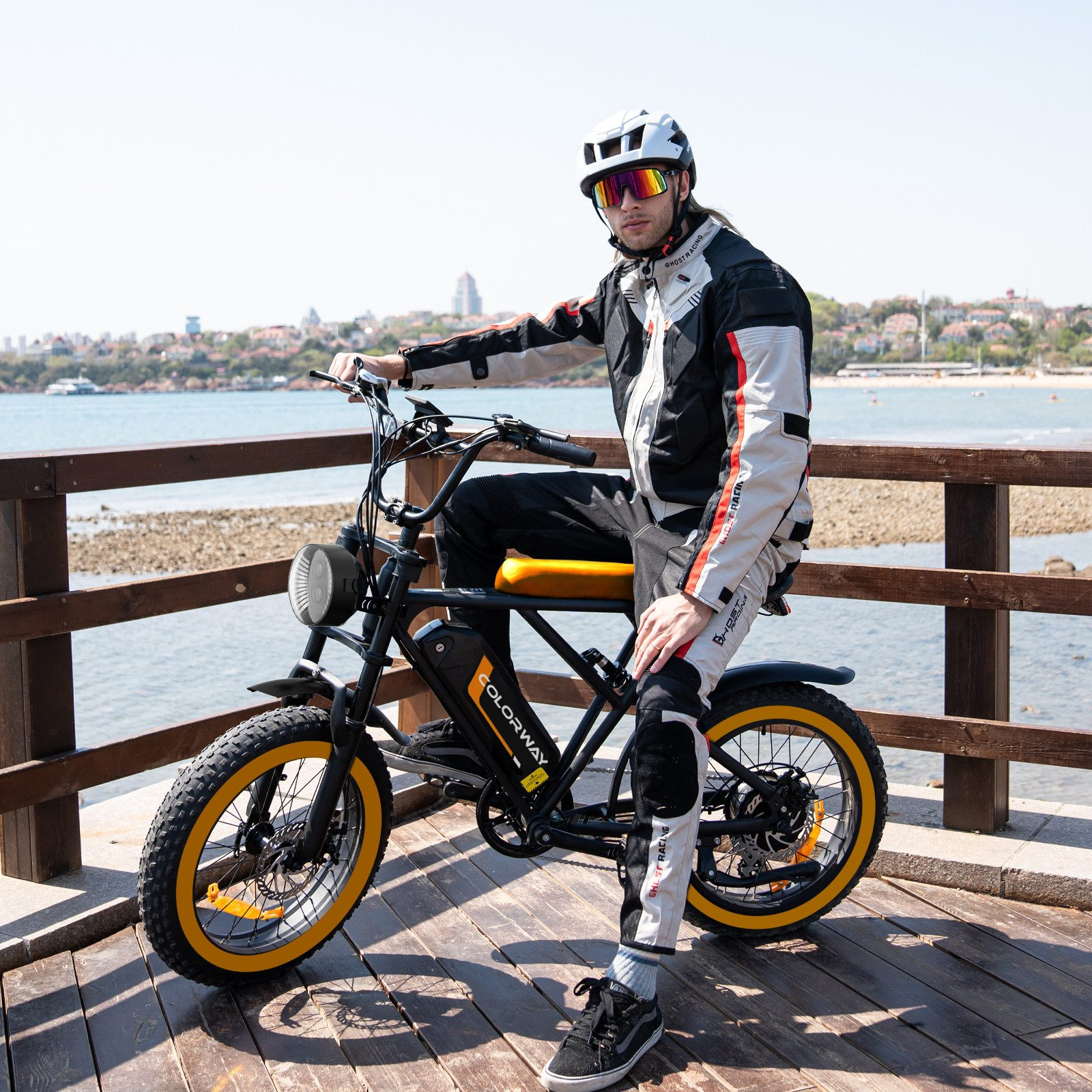 Mann auf einem E-Bike auf einem Holzsteg, mit Küstenhintergrund.