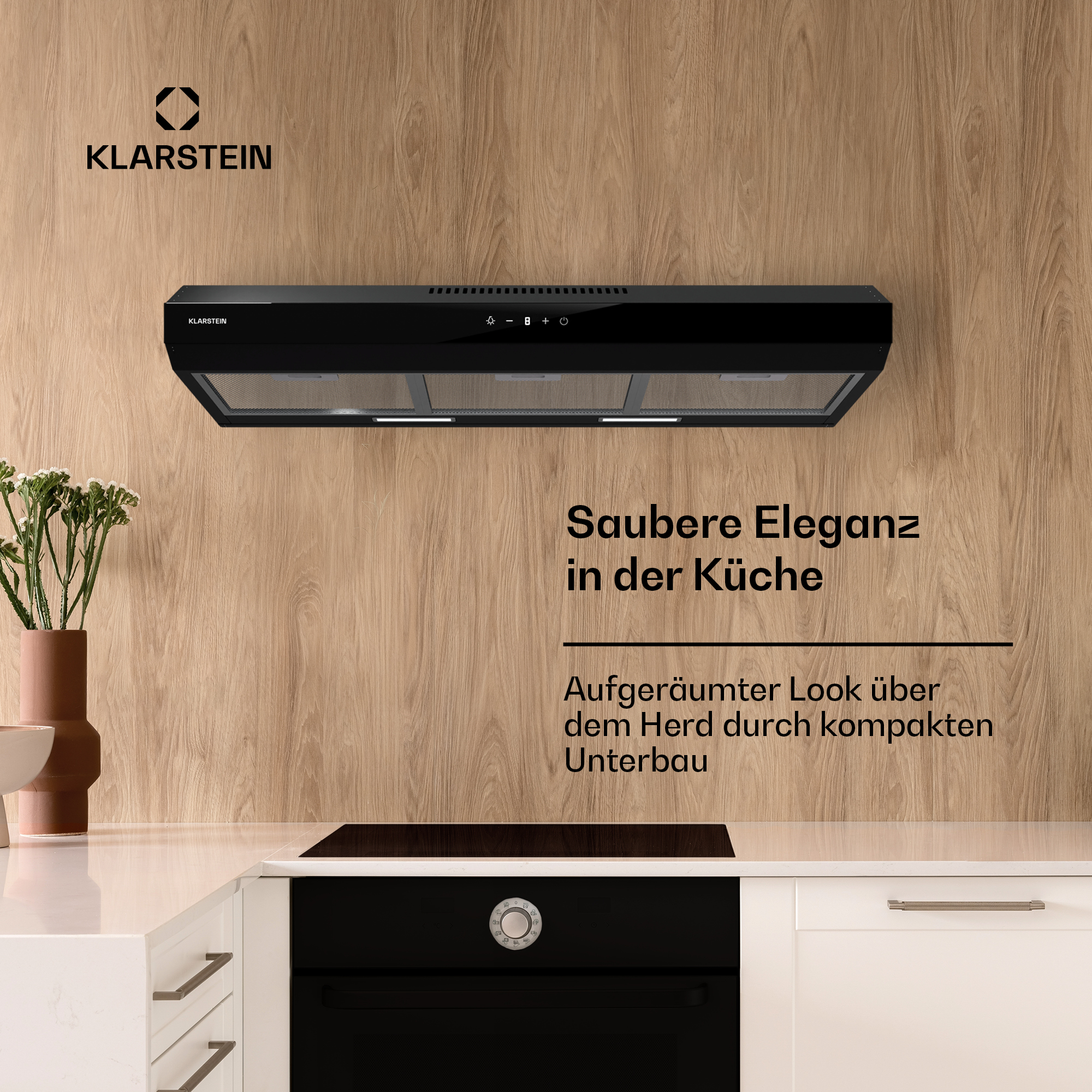 Scena cucina, cappa Klarstein nera sopra fornello, parete legno, mobili bianchi, pianta.