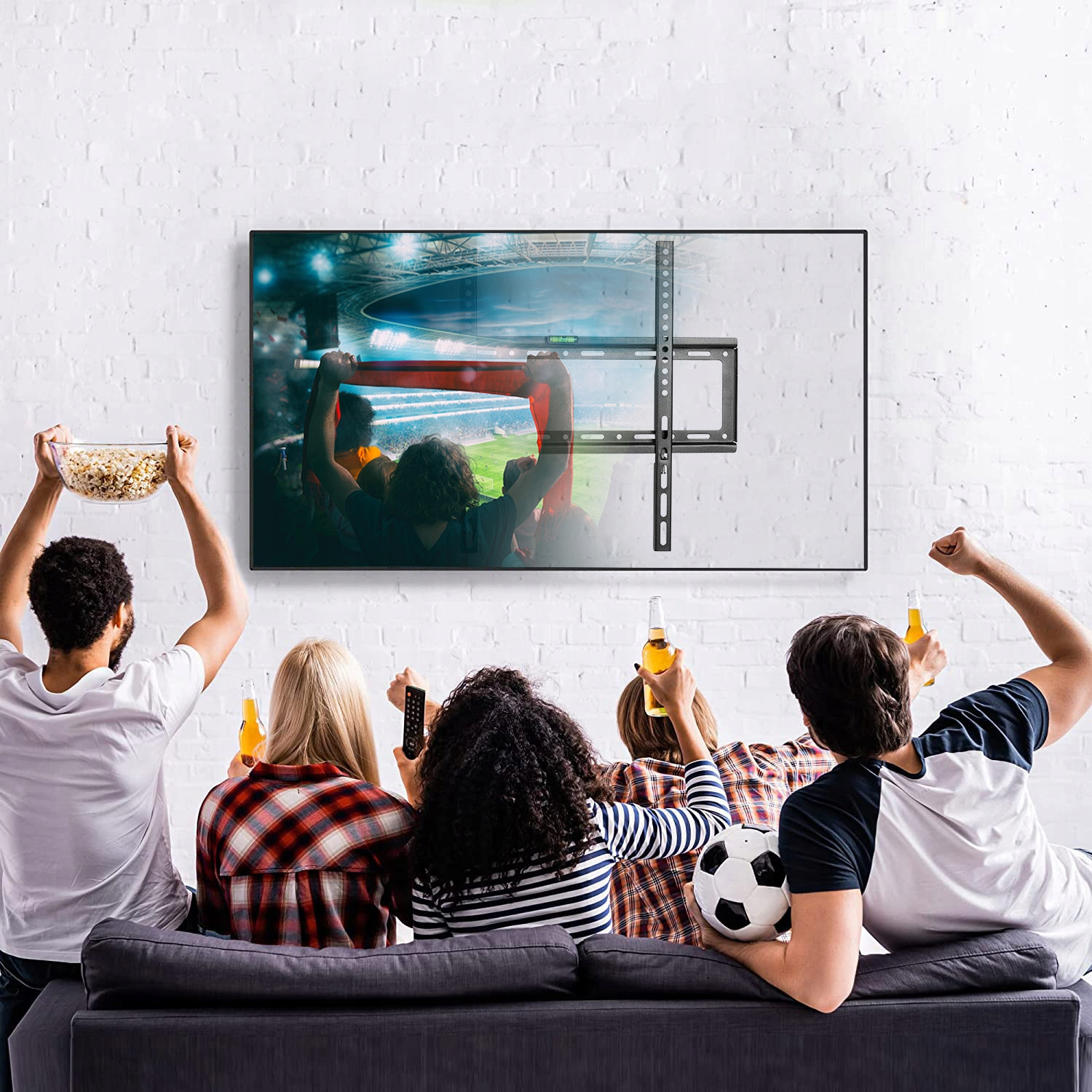 Ludzie oglądają mecz w telewizji zamontowanej na białej ceglanej ścianie. Niektórzy trzymają piwo i popcorn.