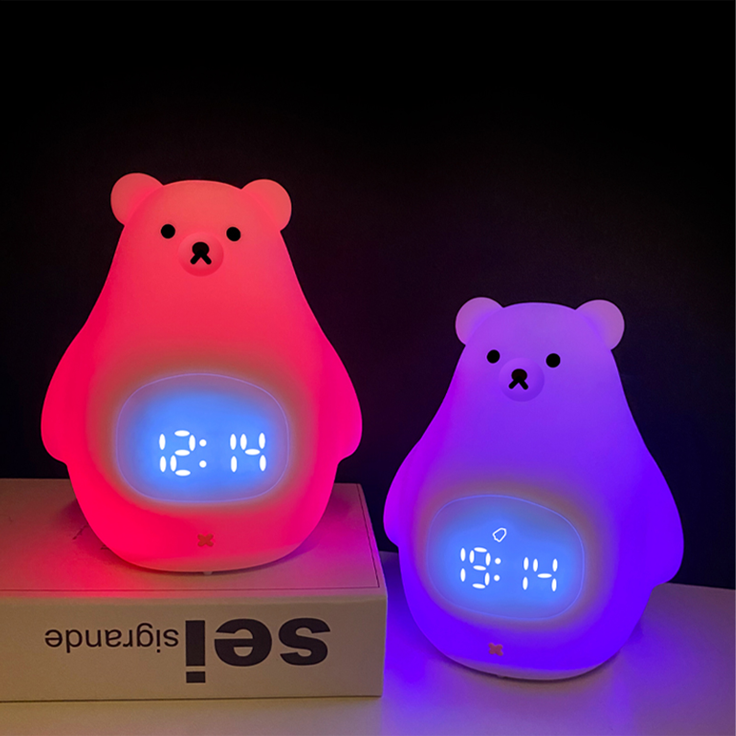 Dos relojes con forma de oso brillando en diferentes colores sobre una superficie blanca.