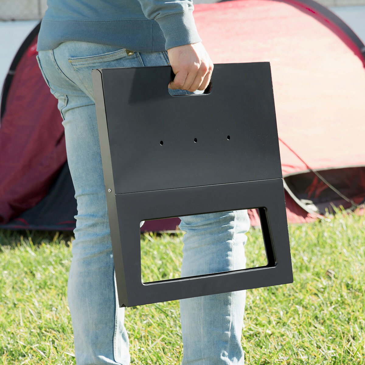 Una persona che tiene un tavolo da grill pieghevole nero davanti a una tenda rossa.