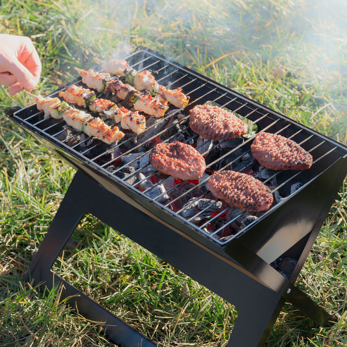 Configurazione barbecue con spiedini e hamburger, con sfondo erboso e luce solare.