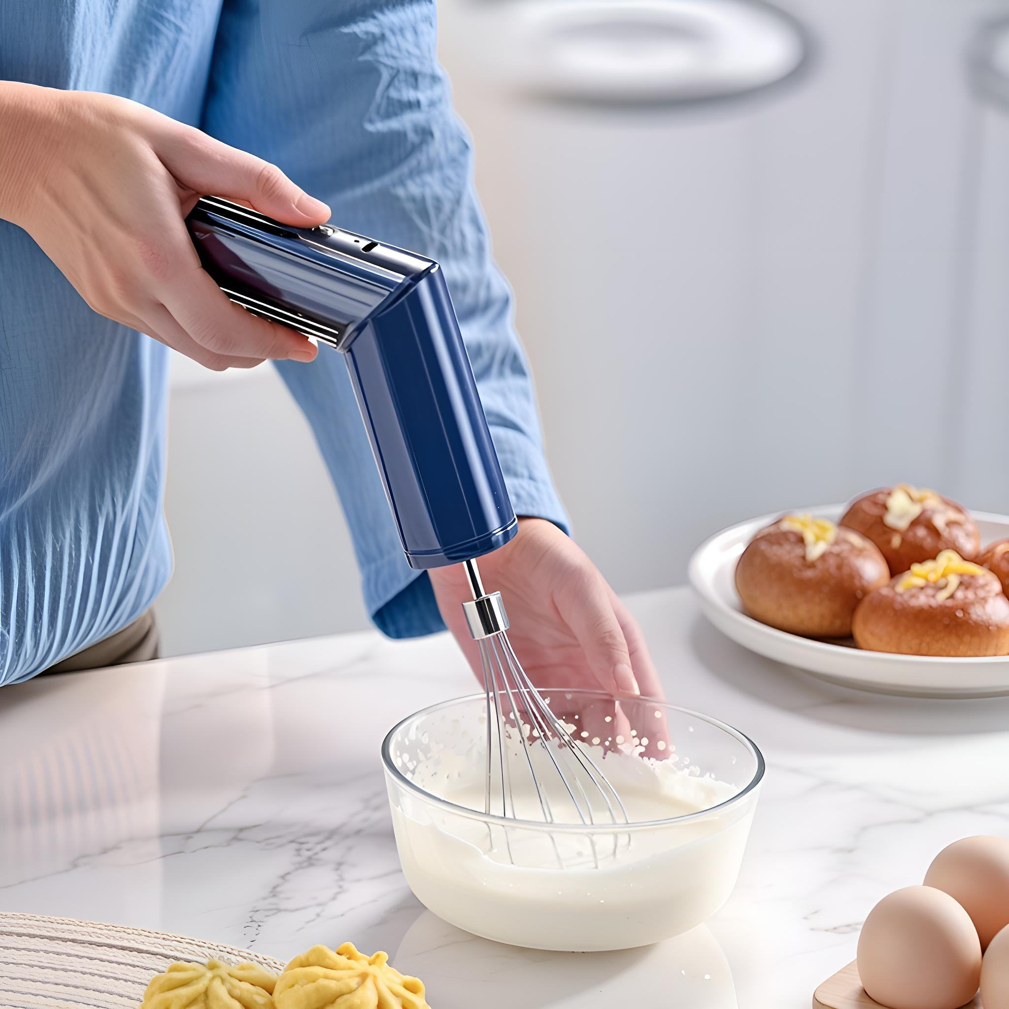 Person benutzt blauen Handmixer, verrührt weiße Creme in Glasschüssel. Brötchen und Eier rechts.