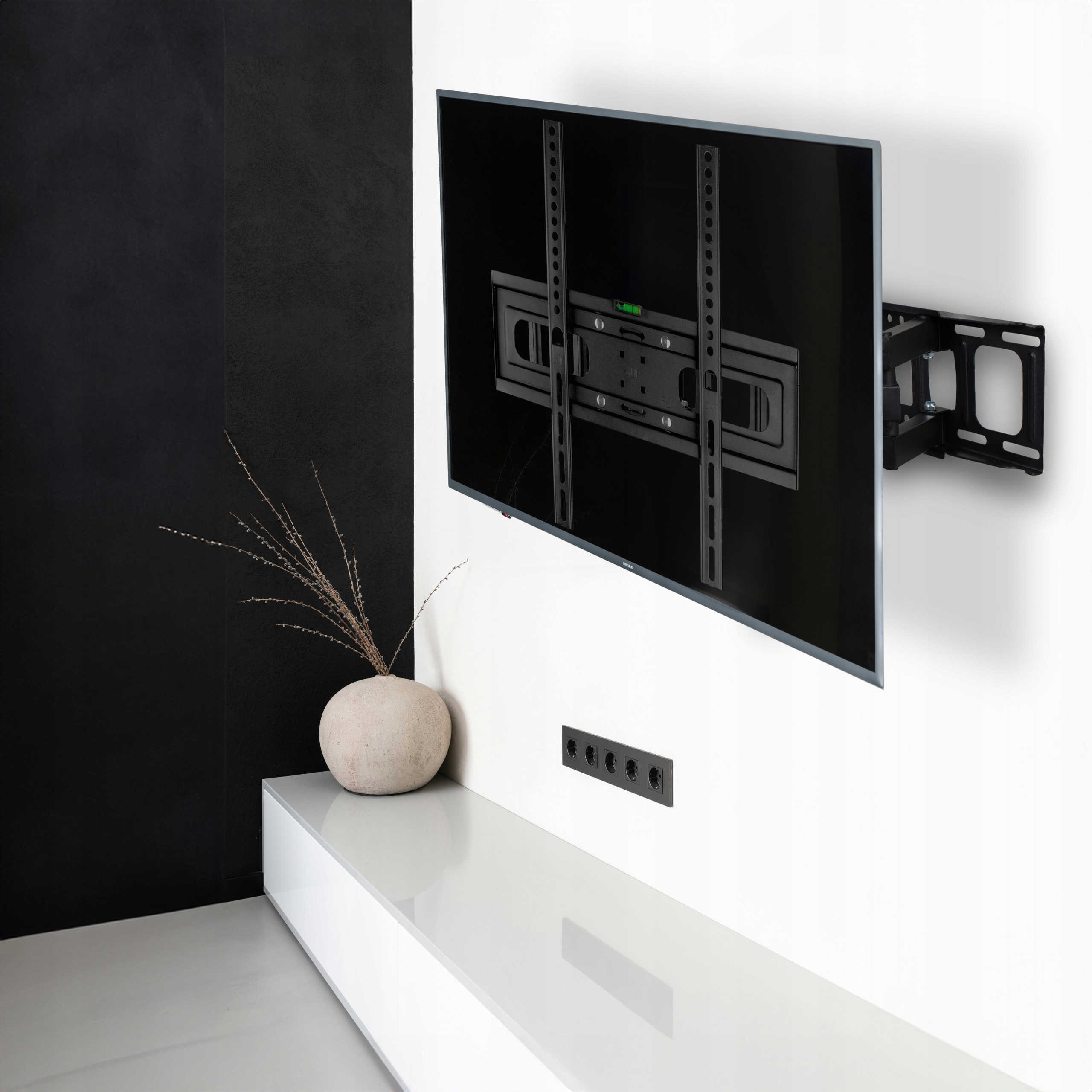 Telewizor zamontowany na czarnym uchwycie ściennym na białej ścianie, nad białą szafką.