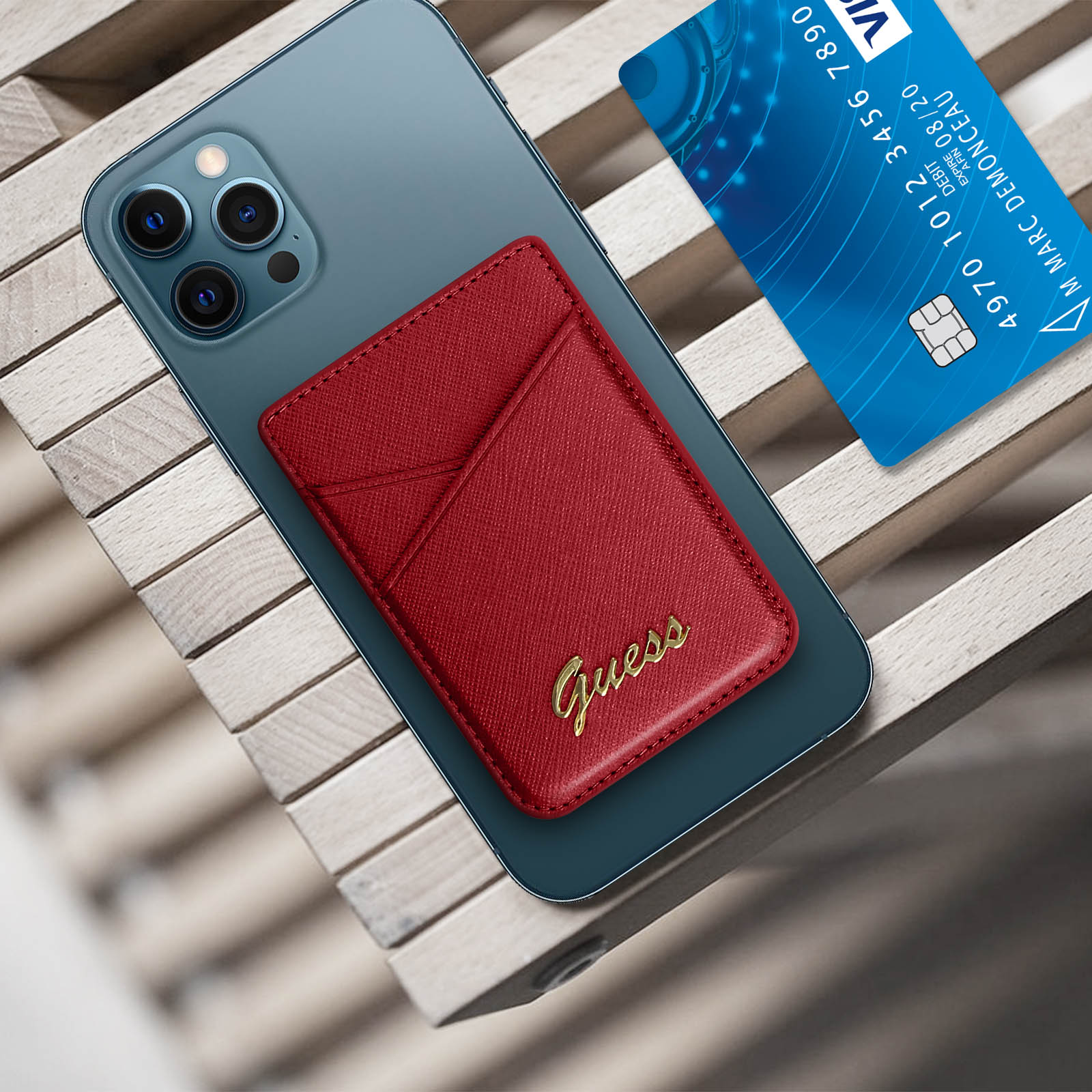 Portafoglio rosso Guess su un telefono, con una carta blu. La carta è su un tavolo di legno.