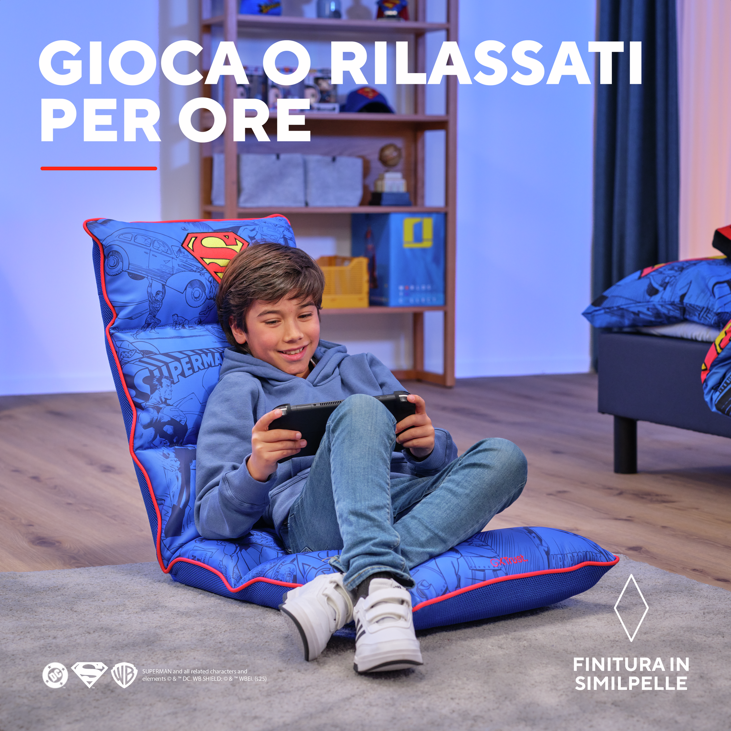 Un bambino gioca su una sedia blu a tema Superman. C'è un letto e degli scaffali sullo sfondo.