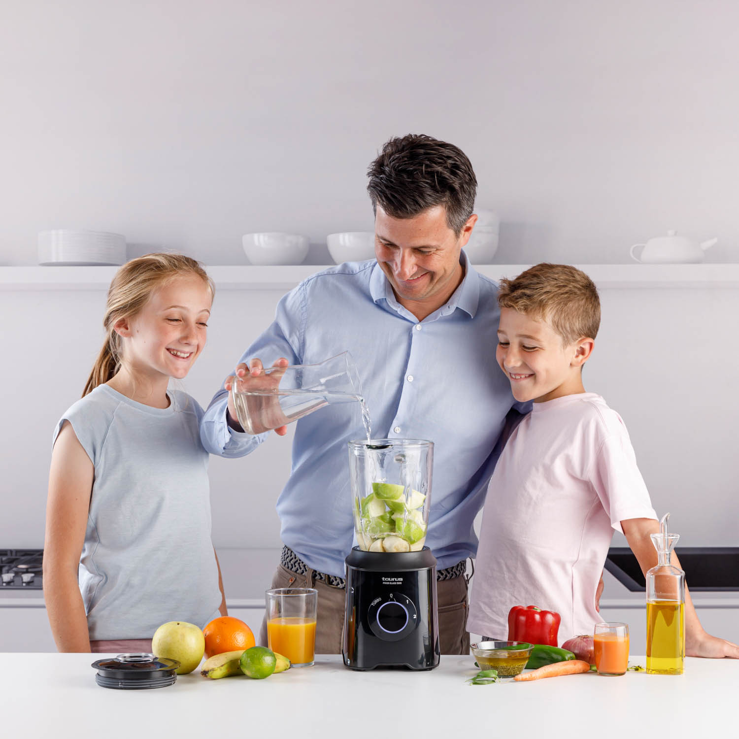 Mężczyzna i dwoje dzieci przygotowują smoothie za pomocą blendera. Owoce i warzywa są na stole.