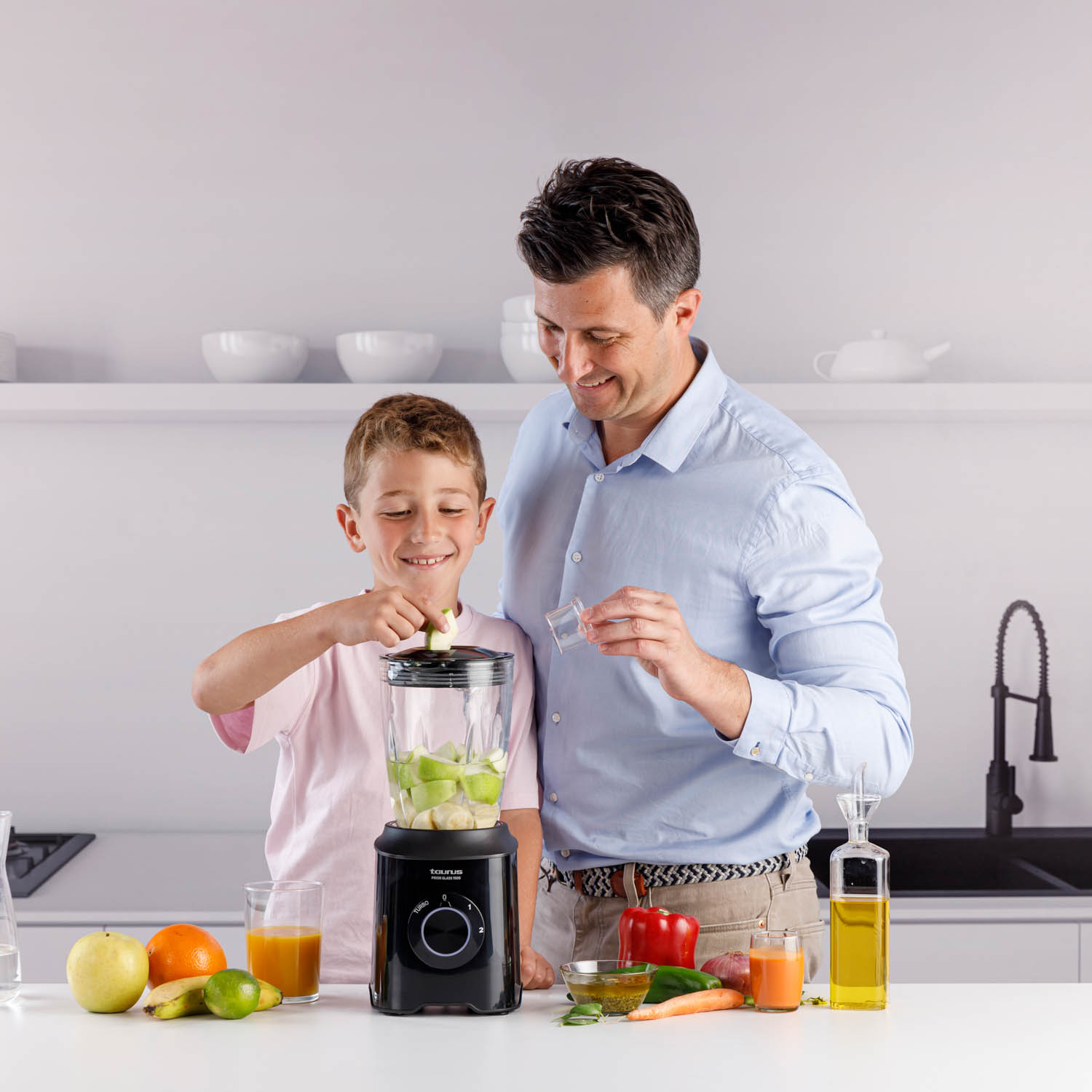 Mężczyzna i chłopiec przygotowują smoothie za pomocą blendera. Owoce i warzywa są na stole.