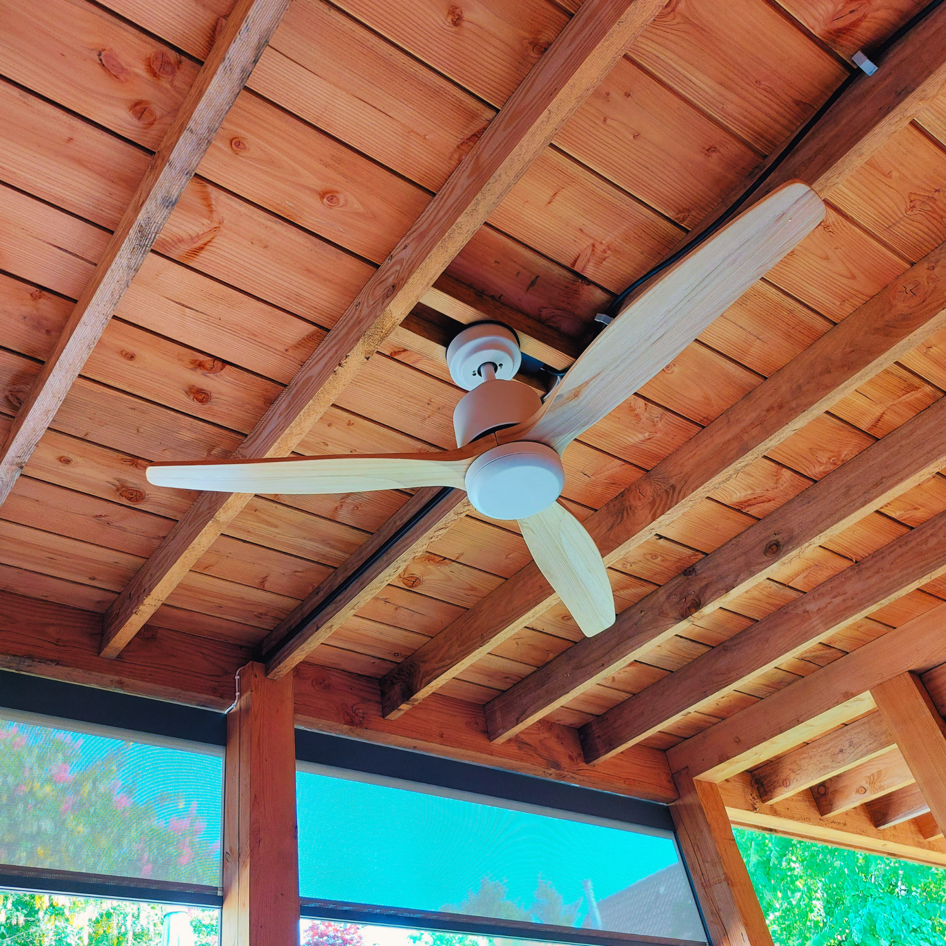 Ventilatore da soffitto su un portico in legno con pale colorate chiare e alloggiamento motore bianco.