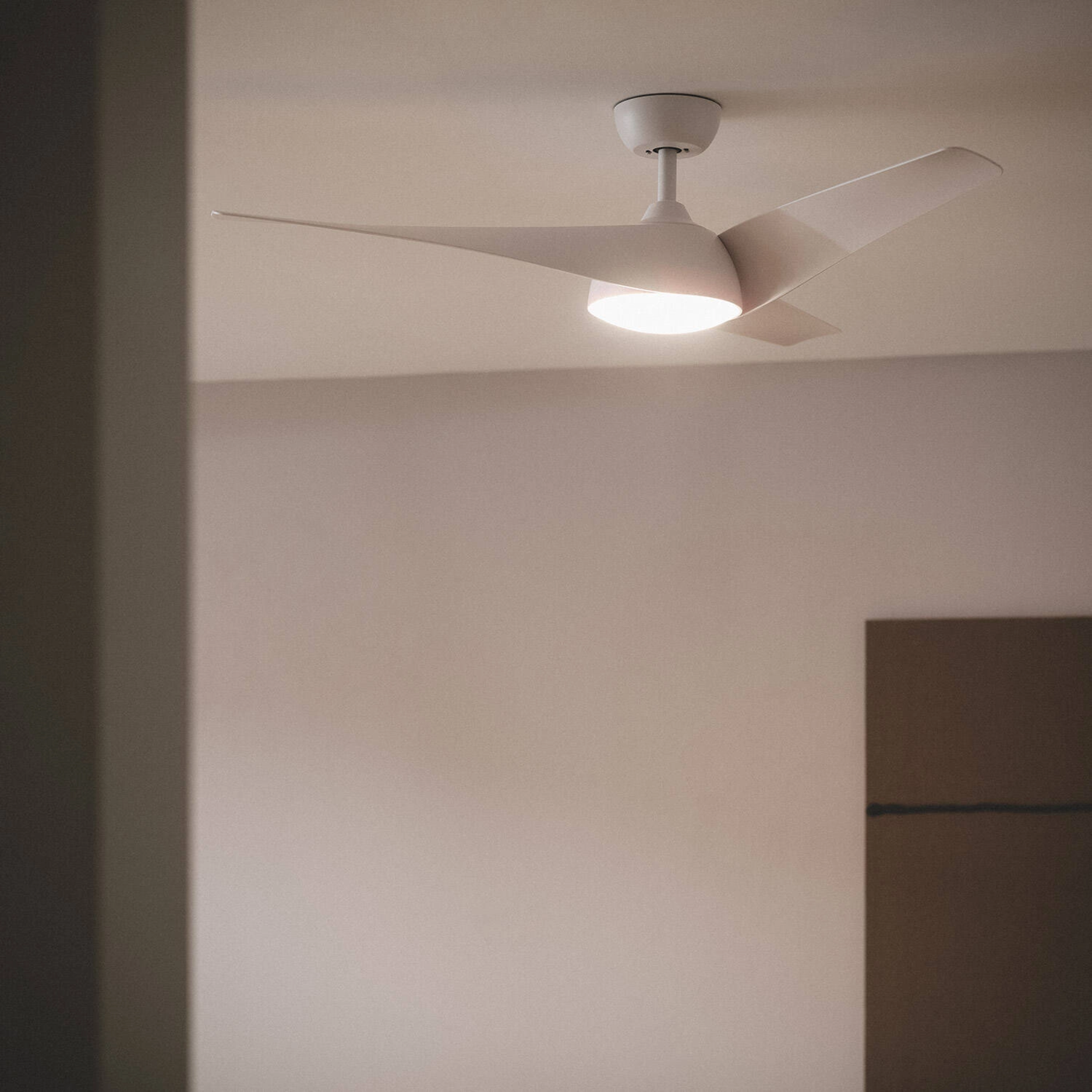 Ventilatore da soffitto bianco con tre pale curve in una stanza, illuminata con luce calda.