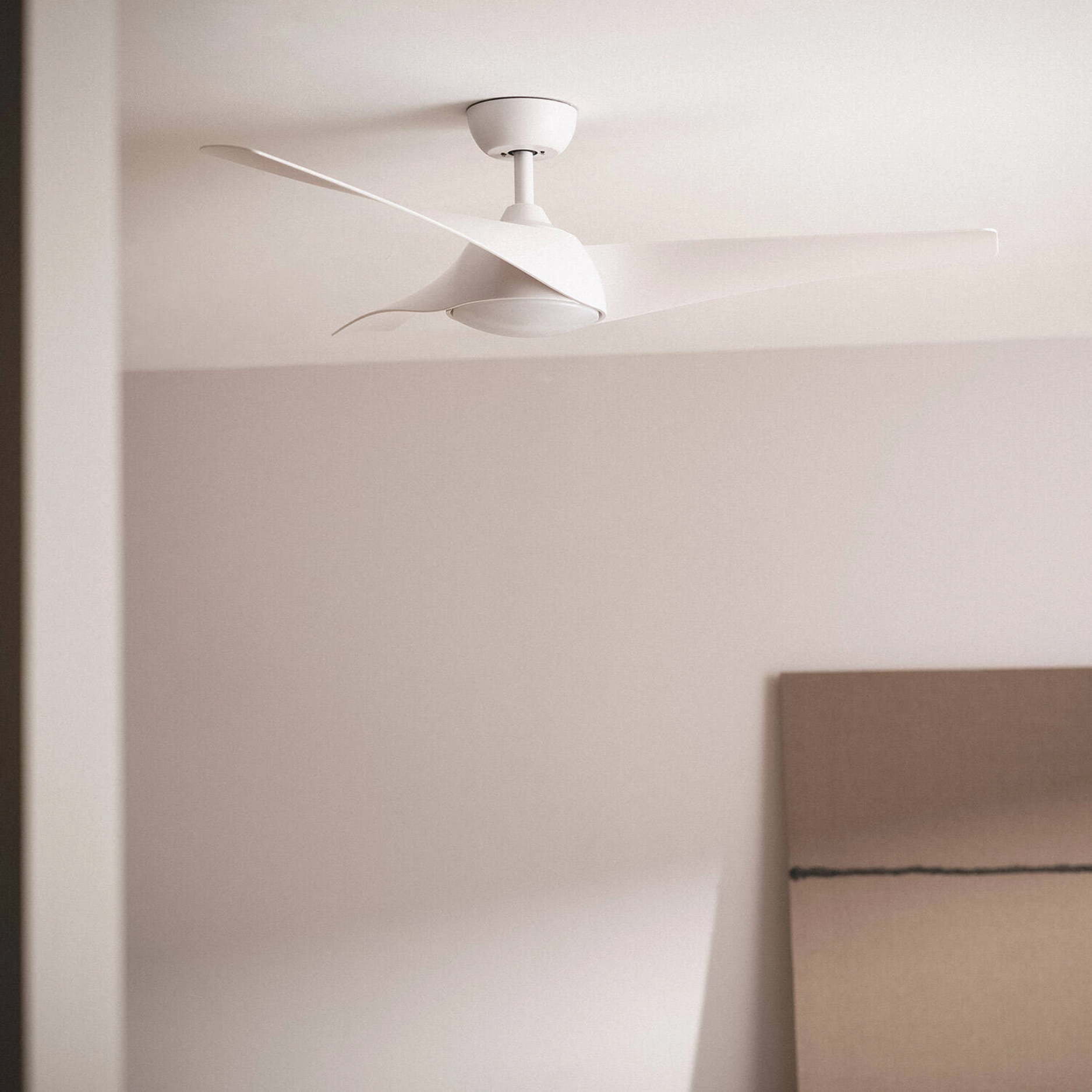 Ventilatore da soffitto bianco con tre pale curve in una stanza moderna con arredi neutri.