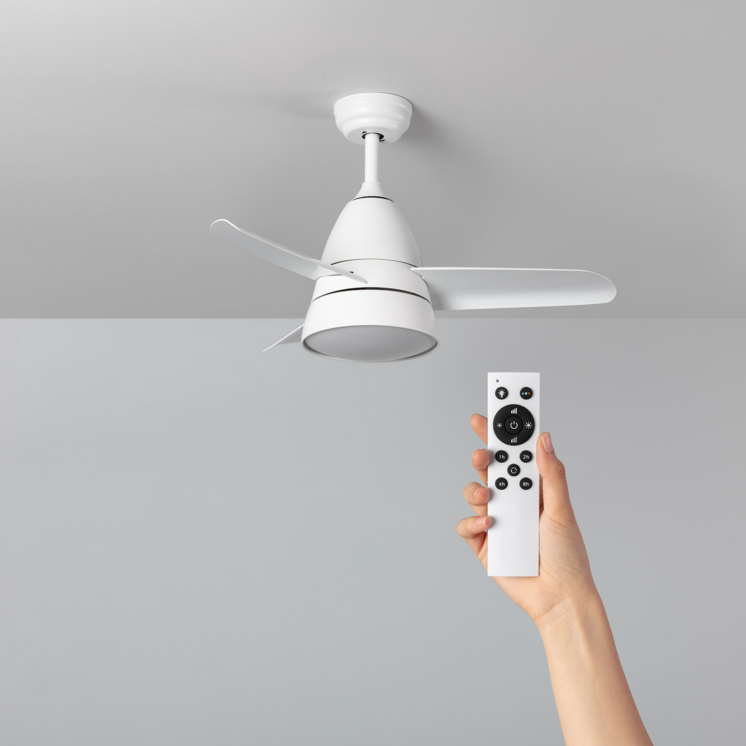 Ventilatore da soffitto bianco e telecomando. Il telecomando è in una mano. Lo sfondo è grigio.