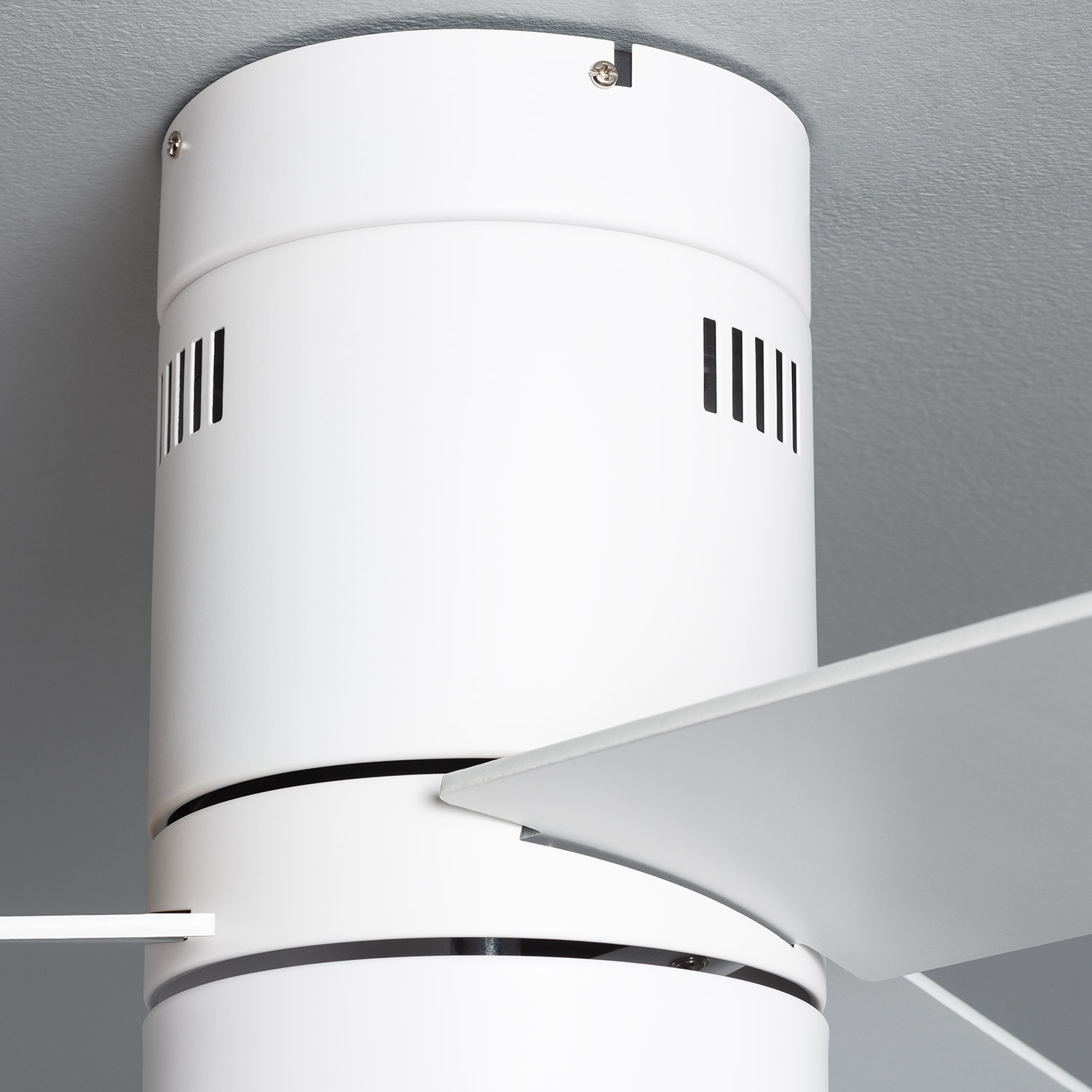 Primo piano dell'alloggiamento del motore e di una pala del ventilatore da soffitto bianco. Lo sfondo è grigio.