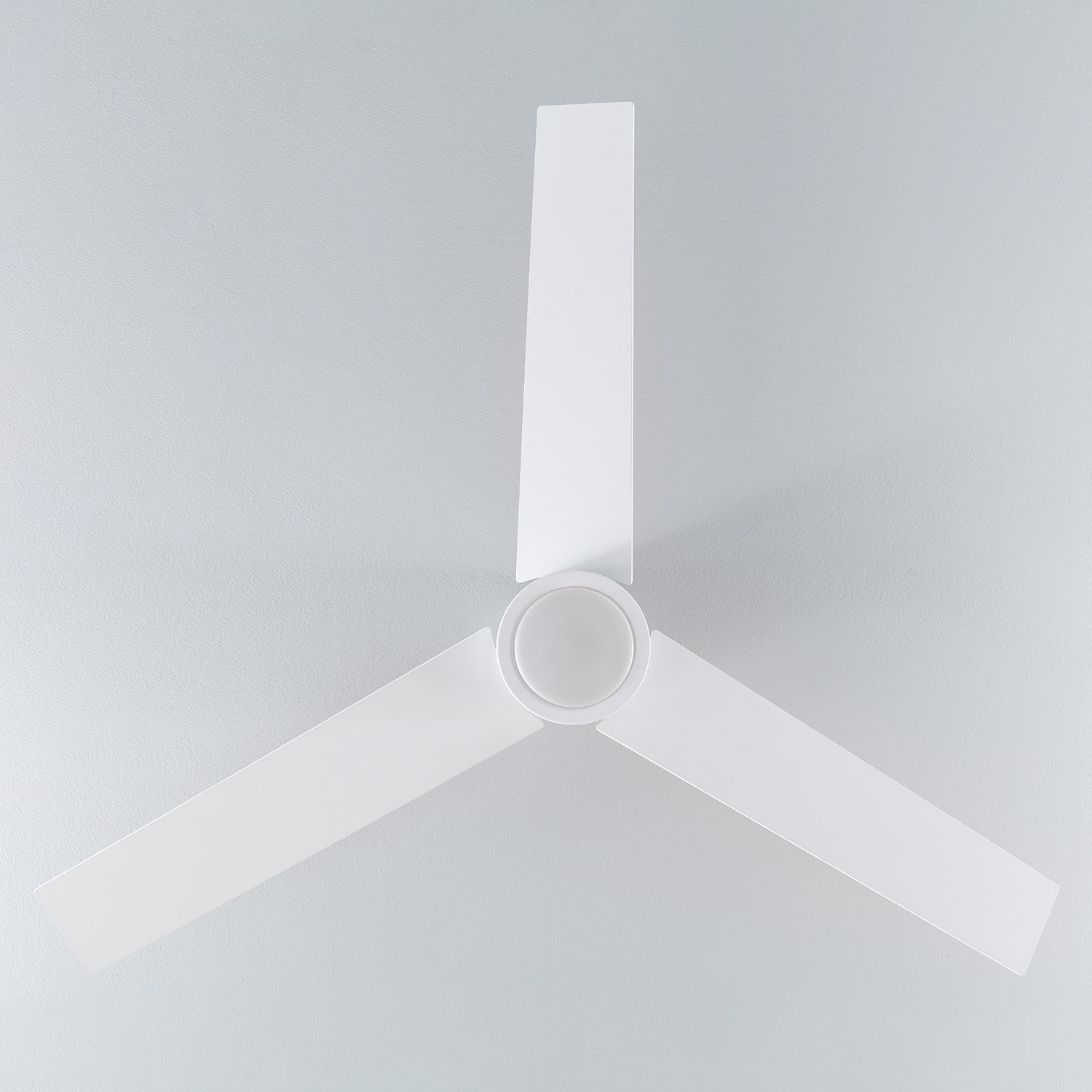 Ventilatore da soffitto bianco con tre pale. Il ventilatore è su uno sfondo grigio. Le pale sono angolate.