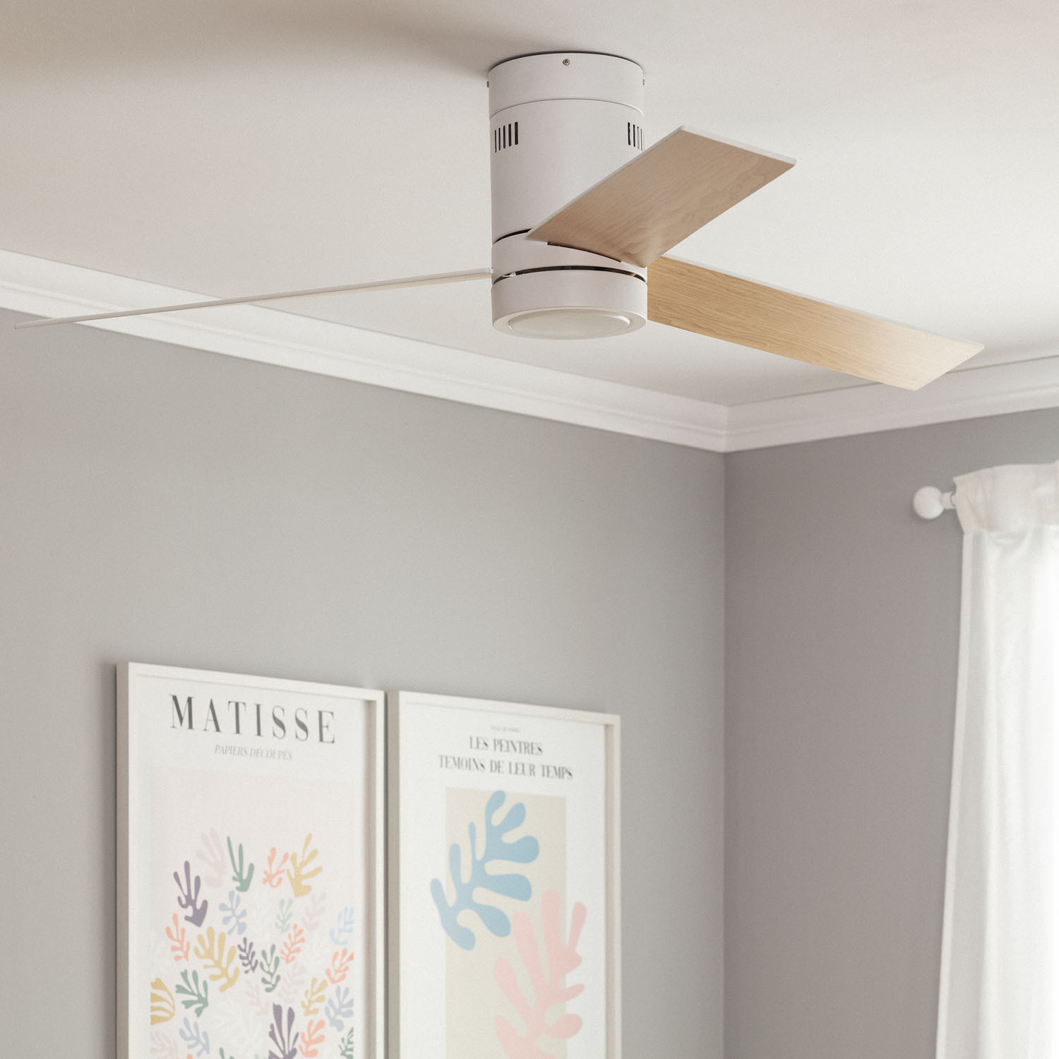 Ventilatore da soffitto bianco con due pale. Il ventilatore è in una stanza con opere d'arte incorniciate e tende bianche.