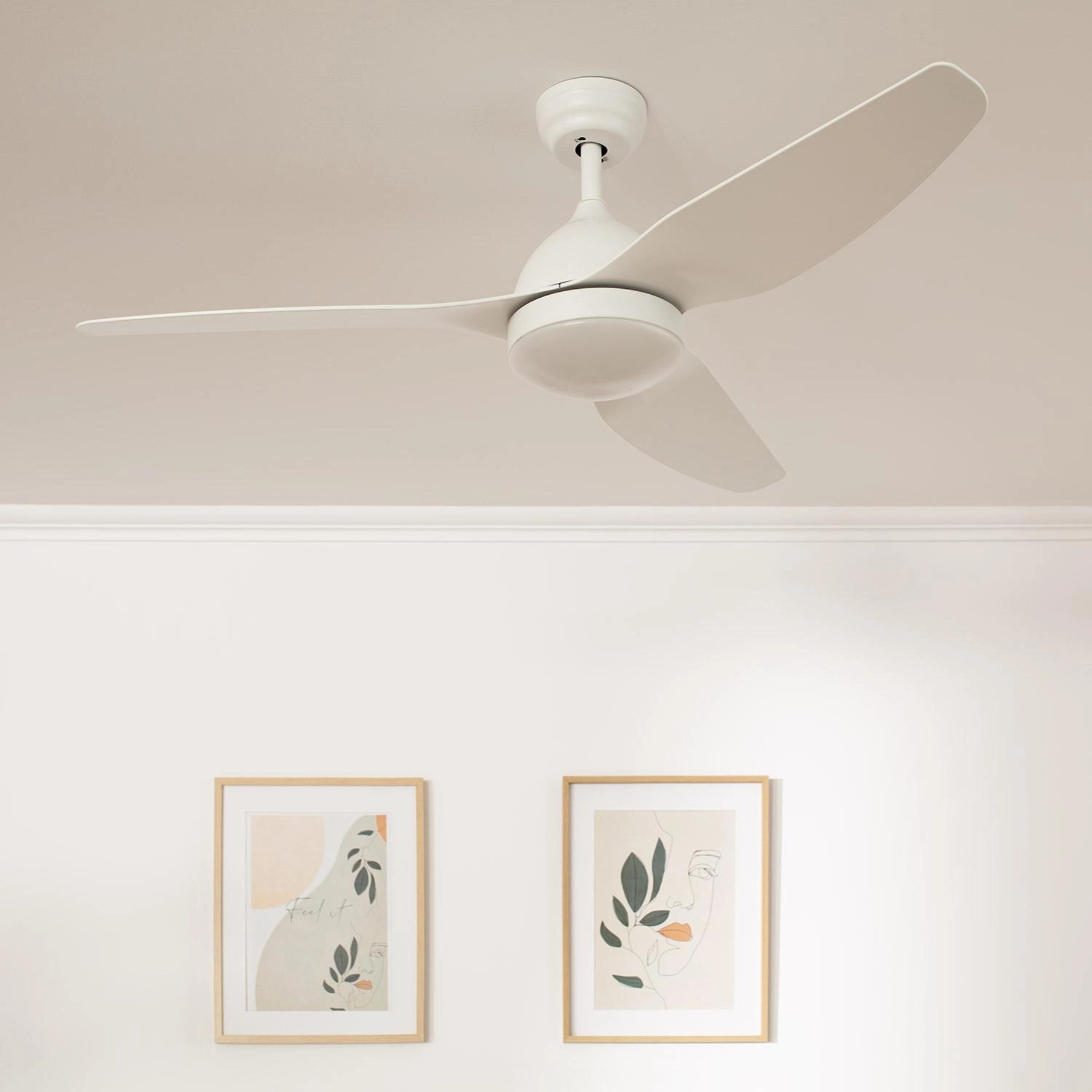 Un ventilatore da soffitto bianco, due opere d'arte incorniciate e pareti bianche. Il ventilatore è centrato.