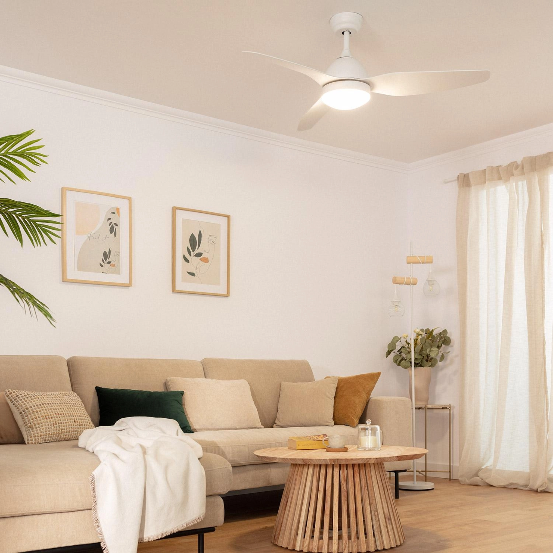 Un soggiorno con un ventilatore da soffitto bianco, un divano, arte, un tavolo e tende. La stanza è luminosa.
