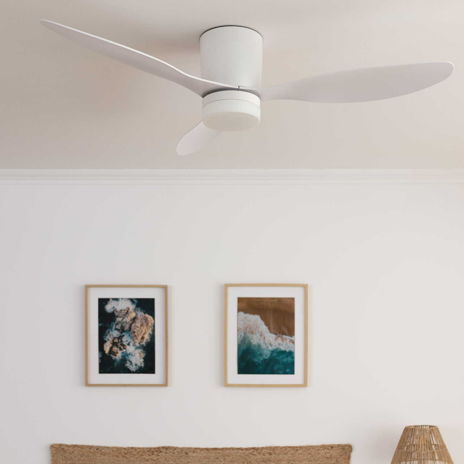 Ventilatore da soffitto bianco a tre pale. Sotto, due immagini incorniciate di spiaggia su un muro bianco.