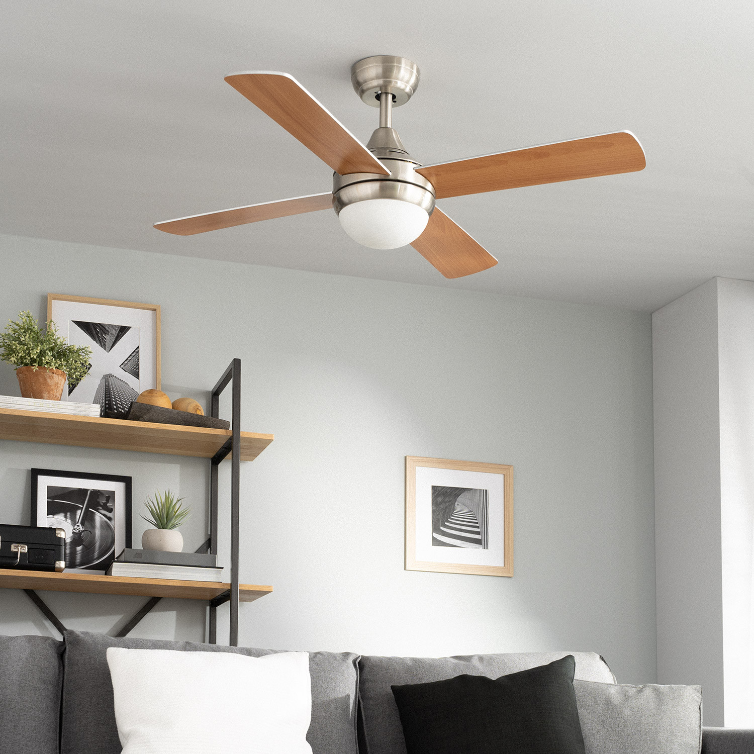 Un ventilatore da soffitto con pale in legno in una stanza. Ci sono quadri, un divano e una mensola sullo sfondo.