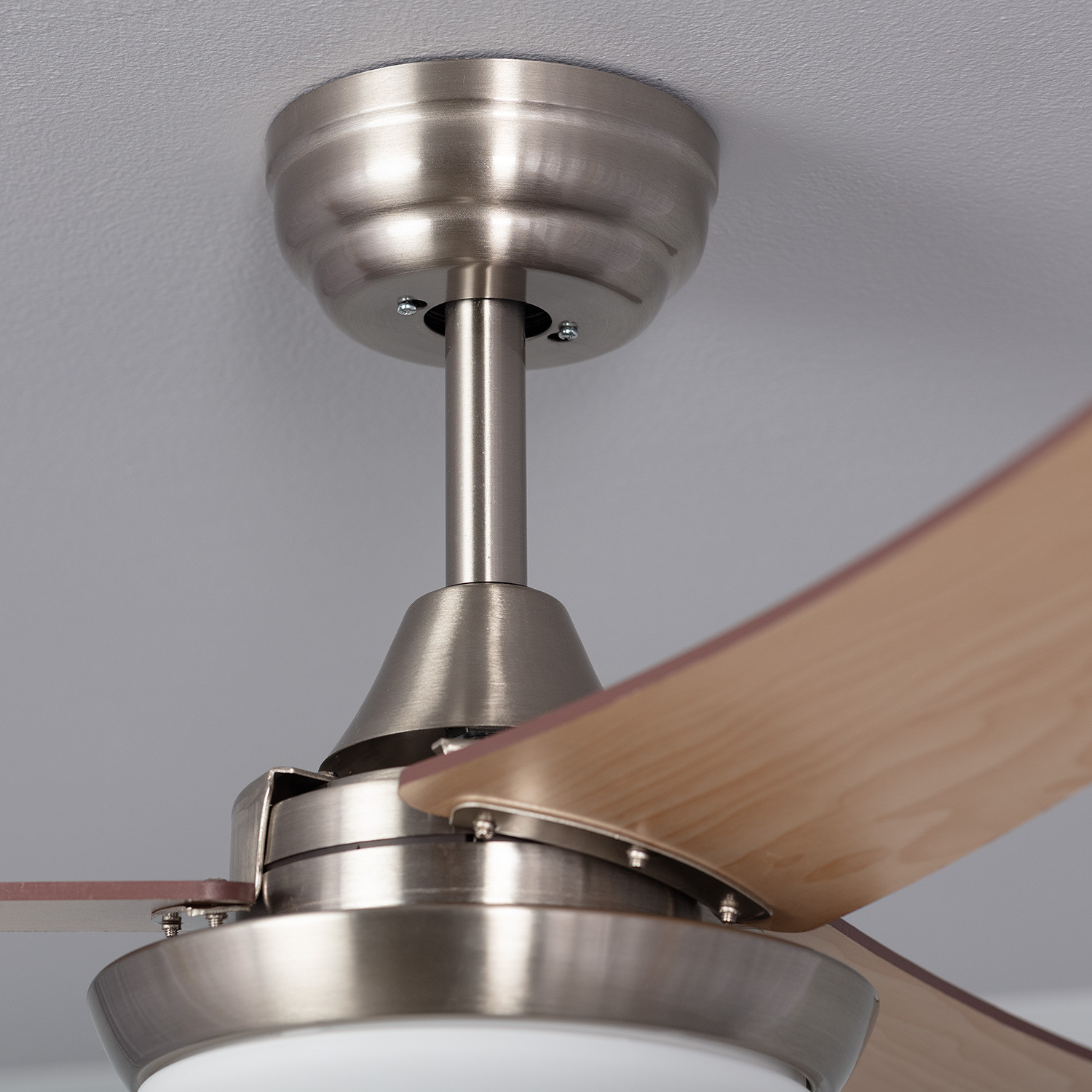 Primo piano del supporto del ventilatore da soffitto. Argento con pale in legno chiaro. Soffitto bianco.