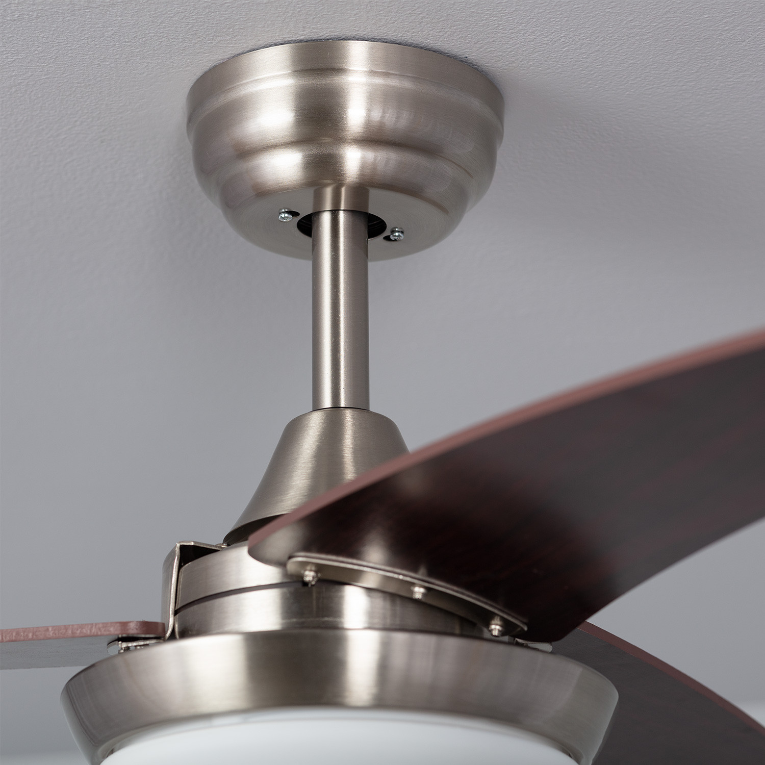 Ventilatore a soffitto con pale argentate e marroni. Le pale sono in legno e la luce è bianca.