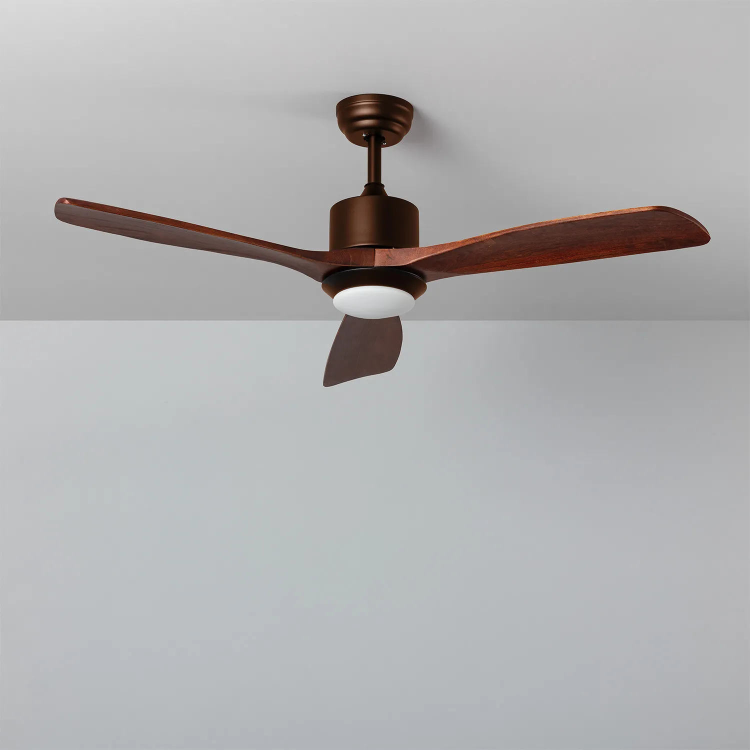 Un ventilatore a soffitto con alloggiamento motore marrone e tre pale in legno scuro su sfondo grigio.