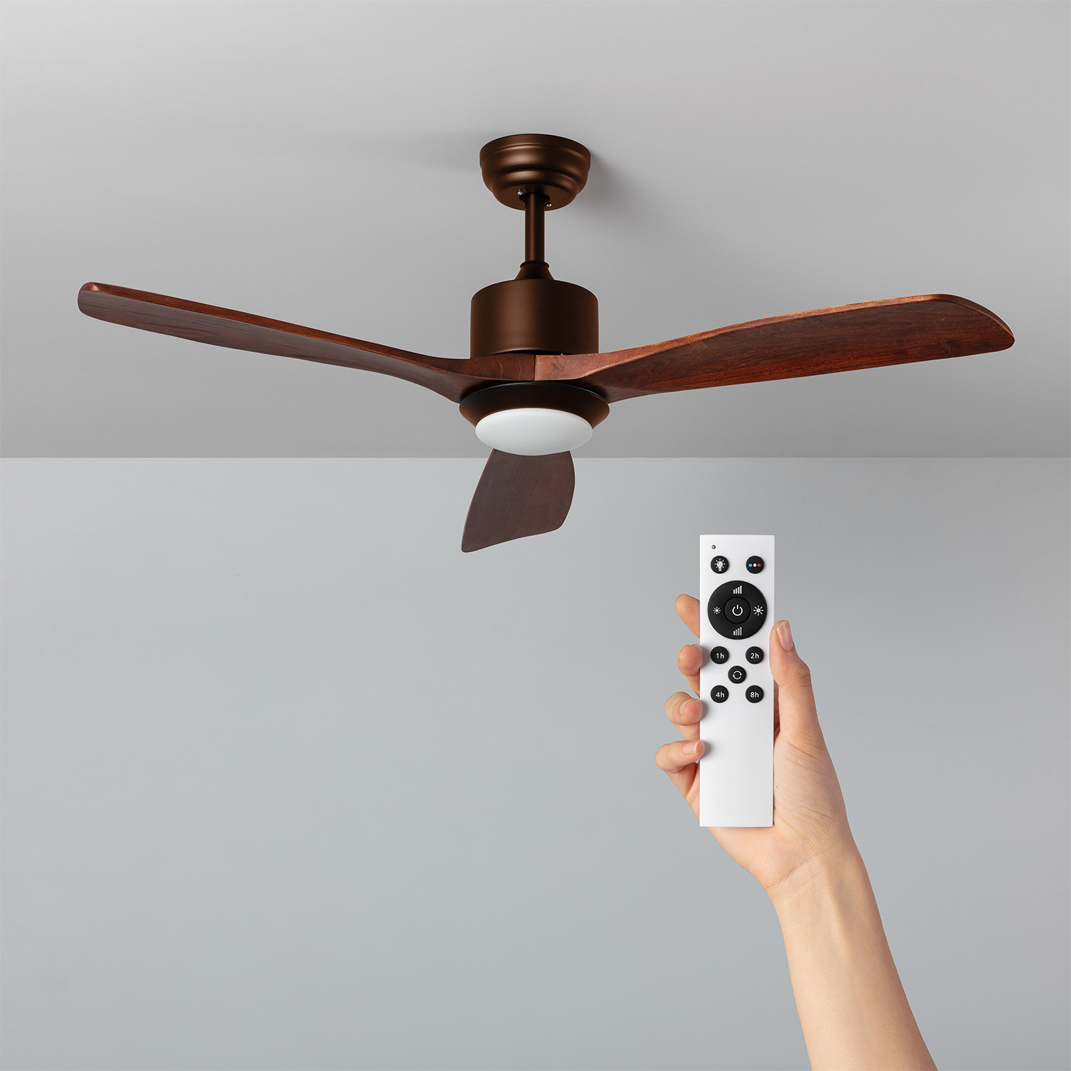 Ventilatore a soffitto con pale marroni, telecomando in mano.