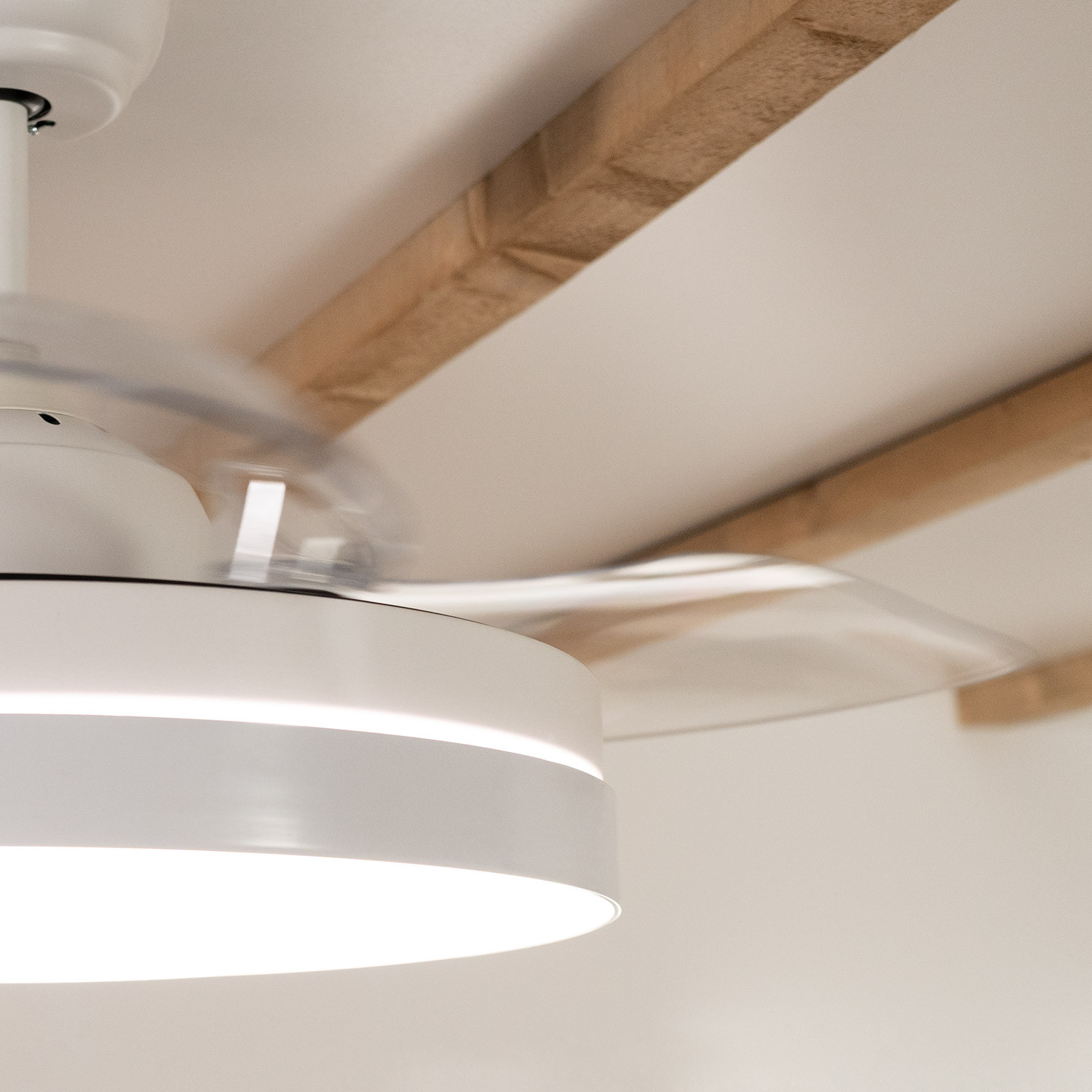 Ventilatore da soffitto bianco con pale in movimento contro soffitto bianco e travi in legno.