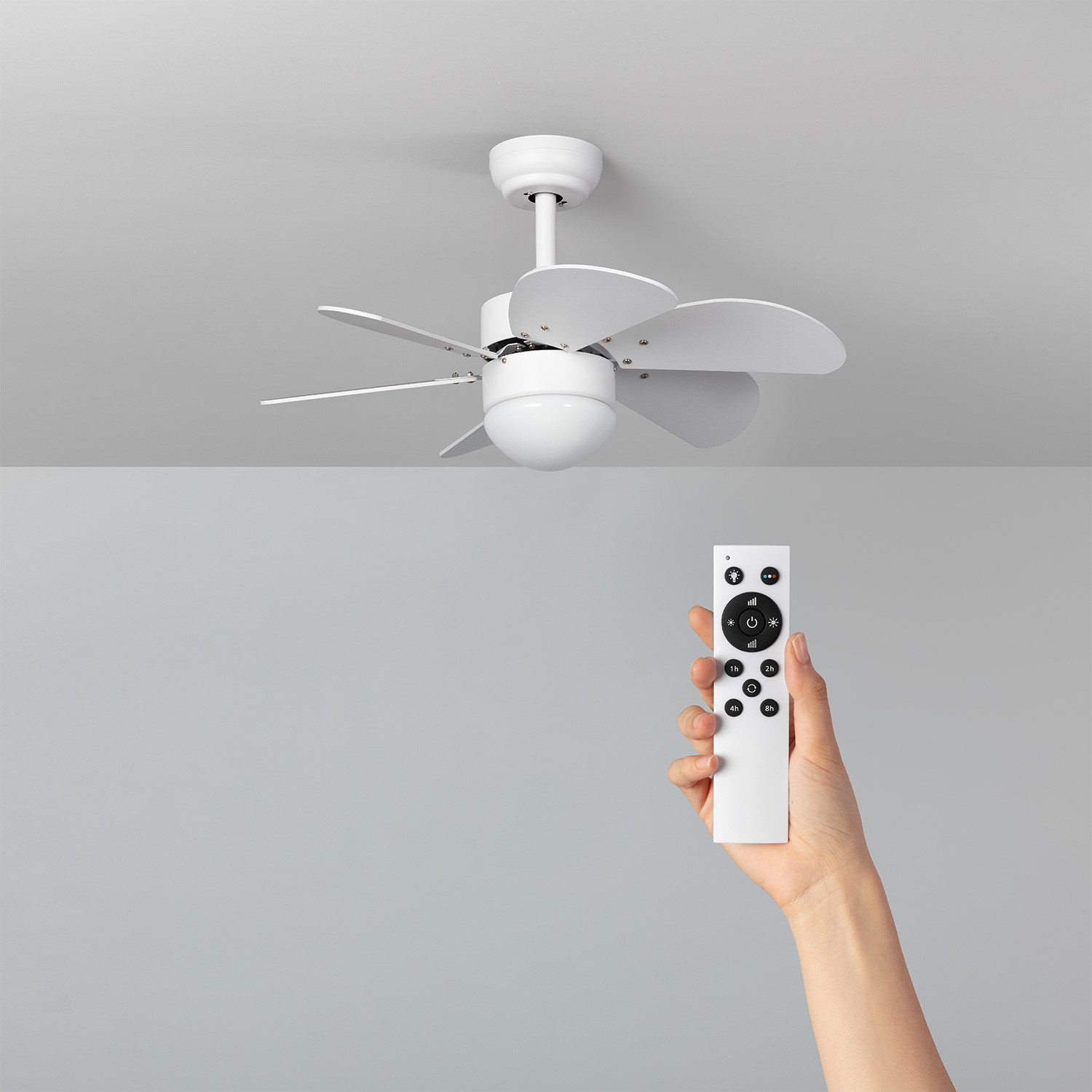 Ventilatore da soffitto bianco con telecomando in mano. Soffitto grigio.
