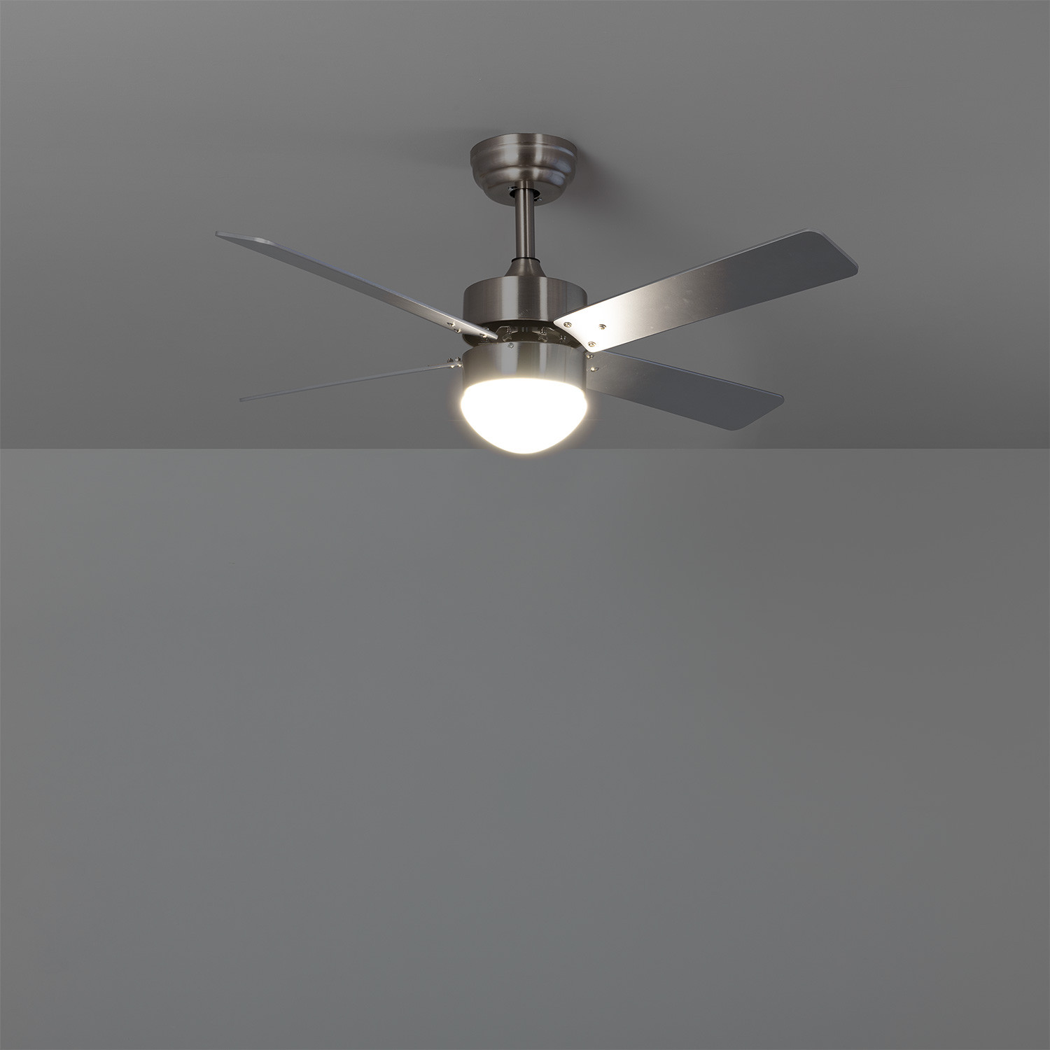 Ventilatore da soffitto con pale e attacco argentati. Sfondo soffitto grigio.