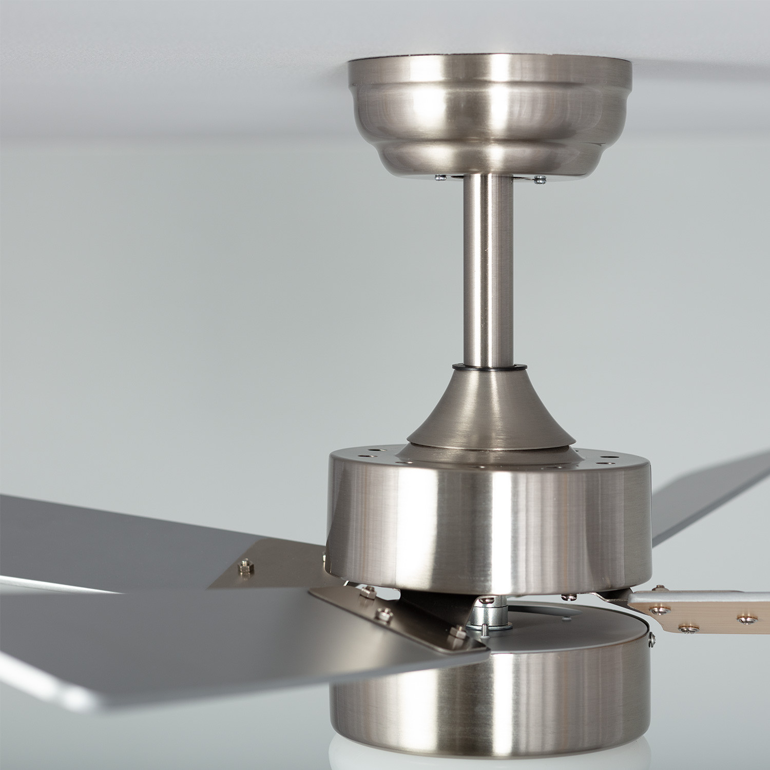 Primo piano del motore e delle pale del ventilatore da soffitto, in argento, fissati al soffitto.