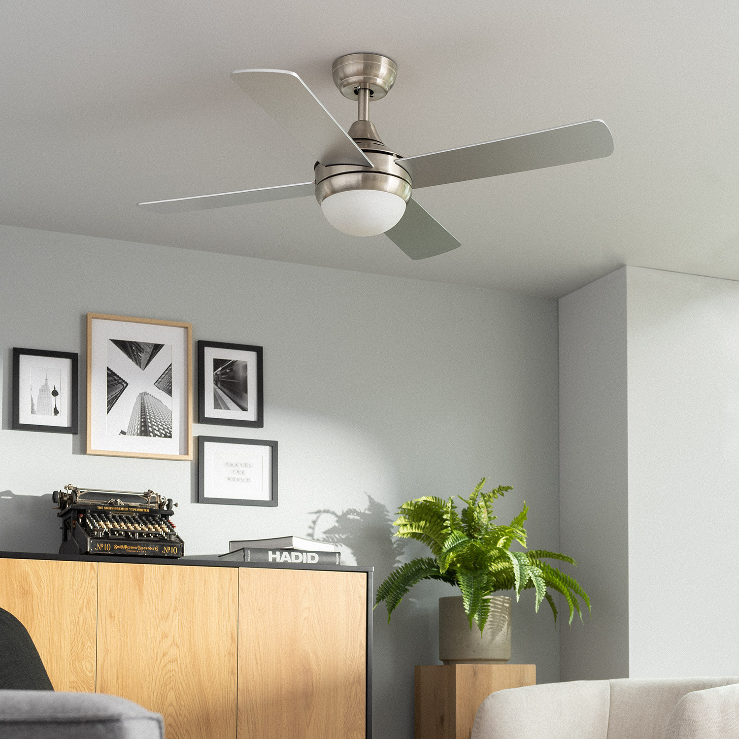 Un ventilatore da soffitto con tre pale argentate e una luce, montato in una stanza grigia.